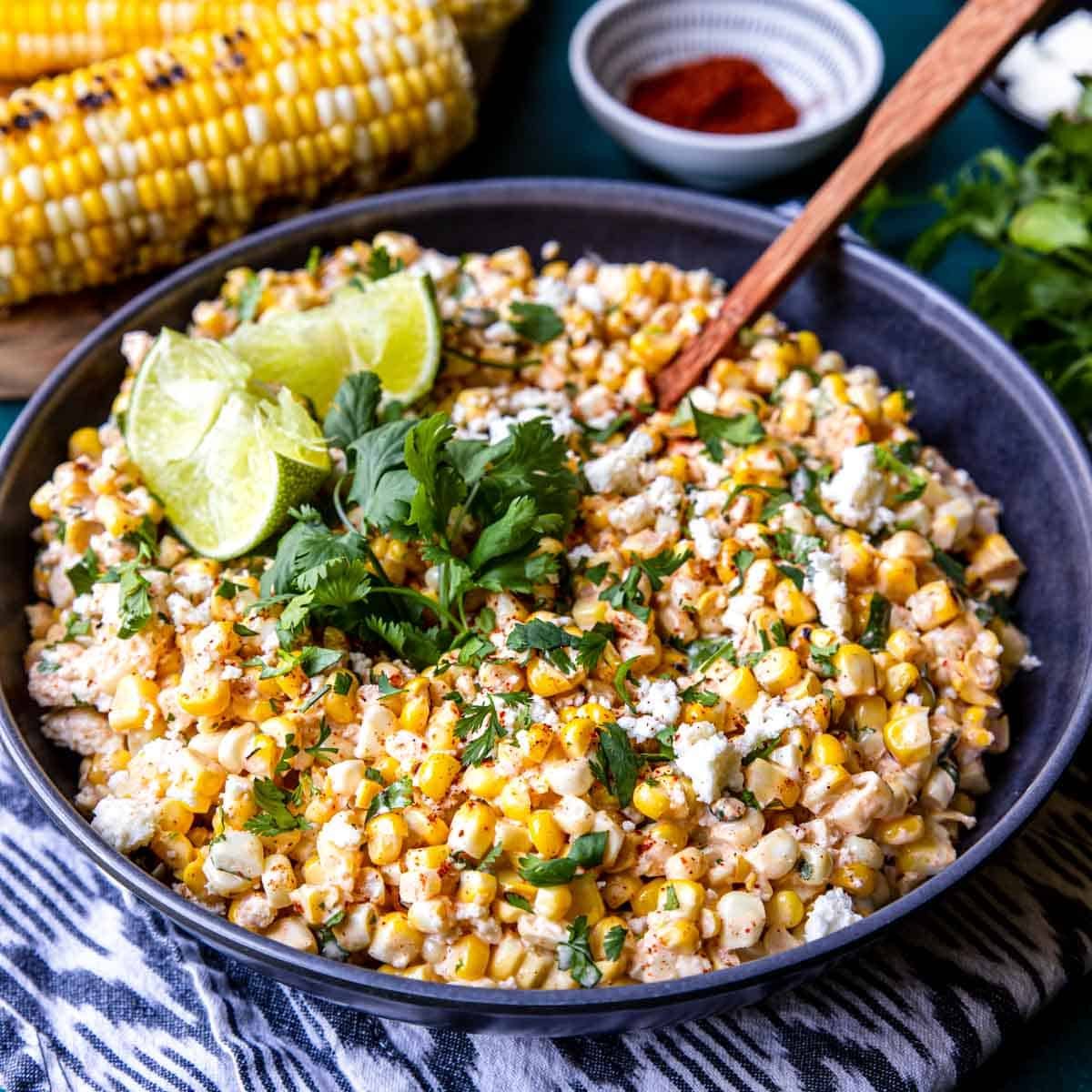 a bowl of Street Corn Salad (aka. Esquites) garnished with limes and cilantro