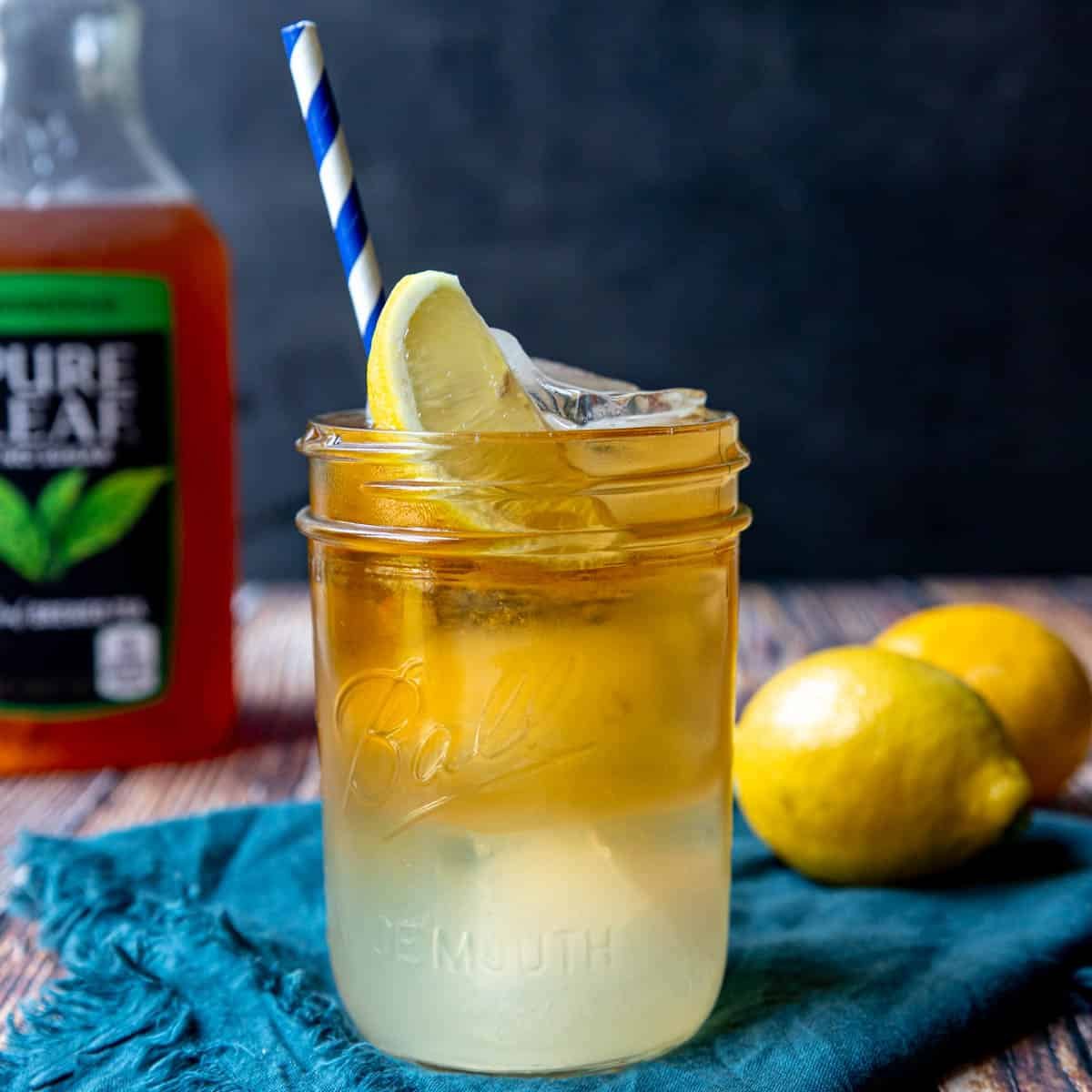 An Arnold Palmer in a glass with a straw and lemon wedge