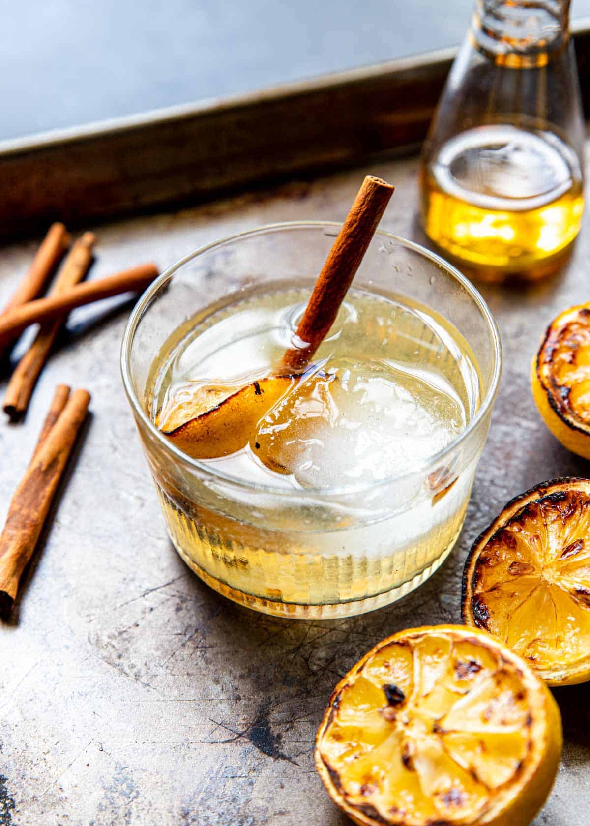 grilled lemon and tequila in a glass with a large ice cube and a cinnamon stick