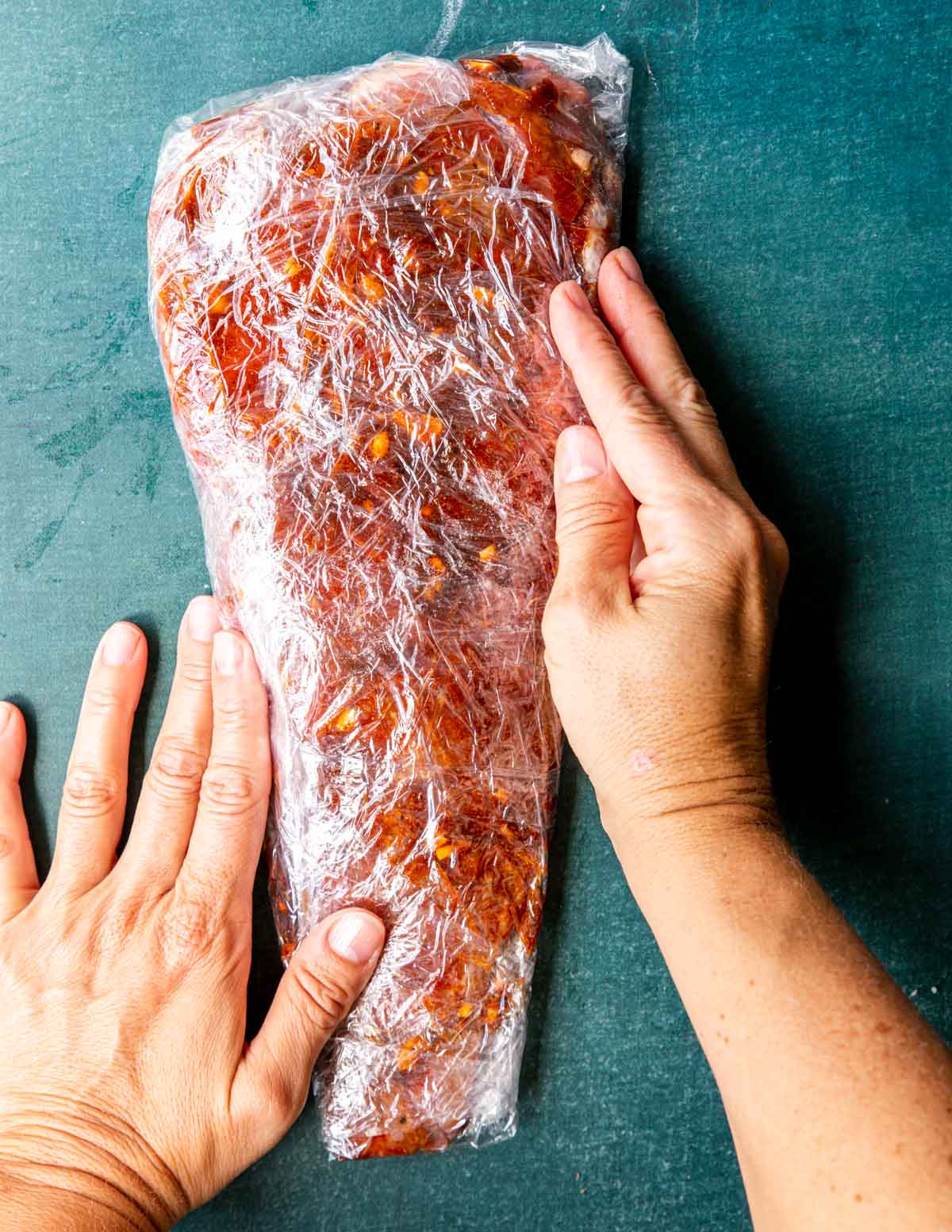 a tri tip coated in marinade and wrapped in plastic wrap.