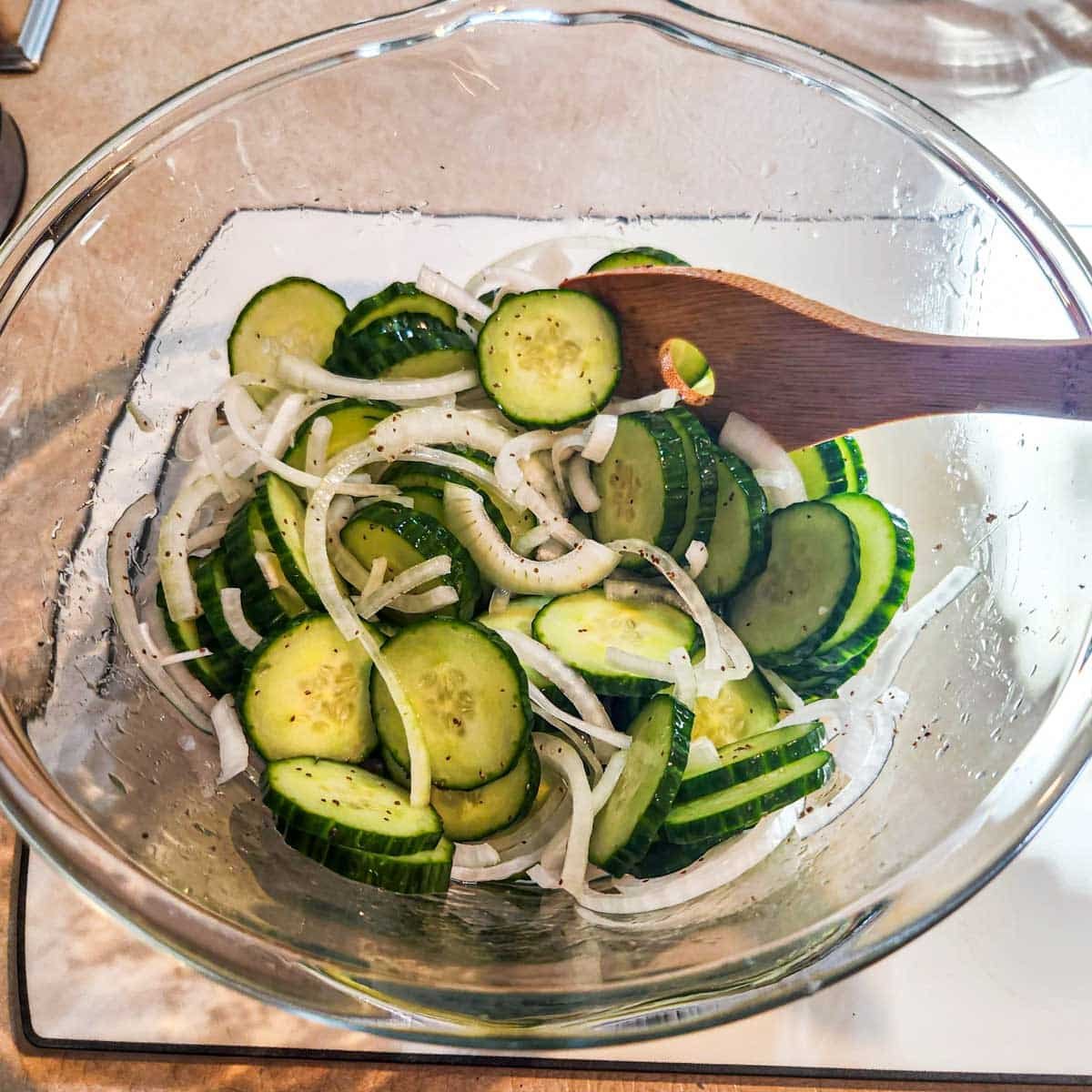 sliced cucumbers and sliced onions in a bowl coated in a vinegar and celery seed mixture