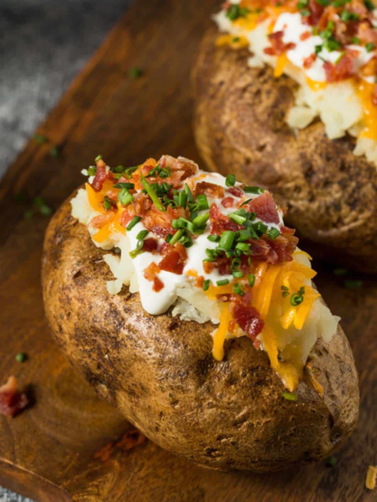 two baked potatoes cut open and stuffed with sour cream, cheese and bacon