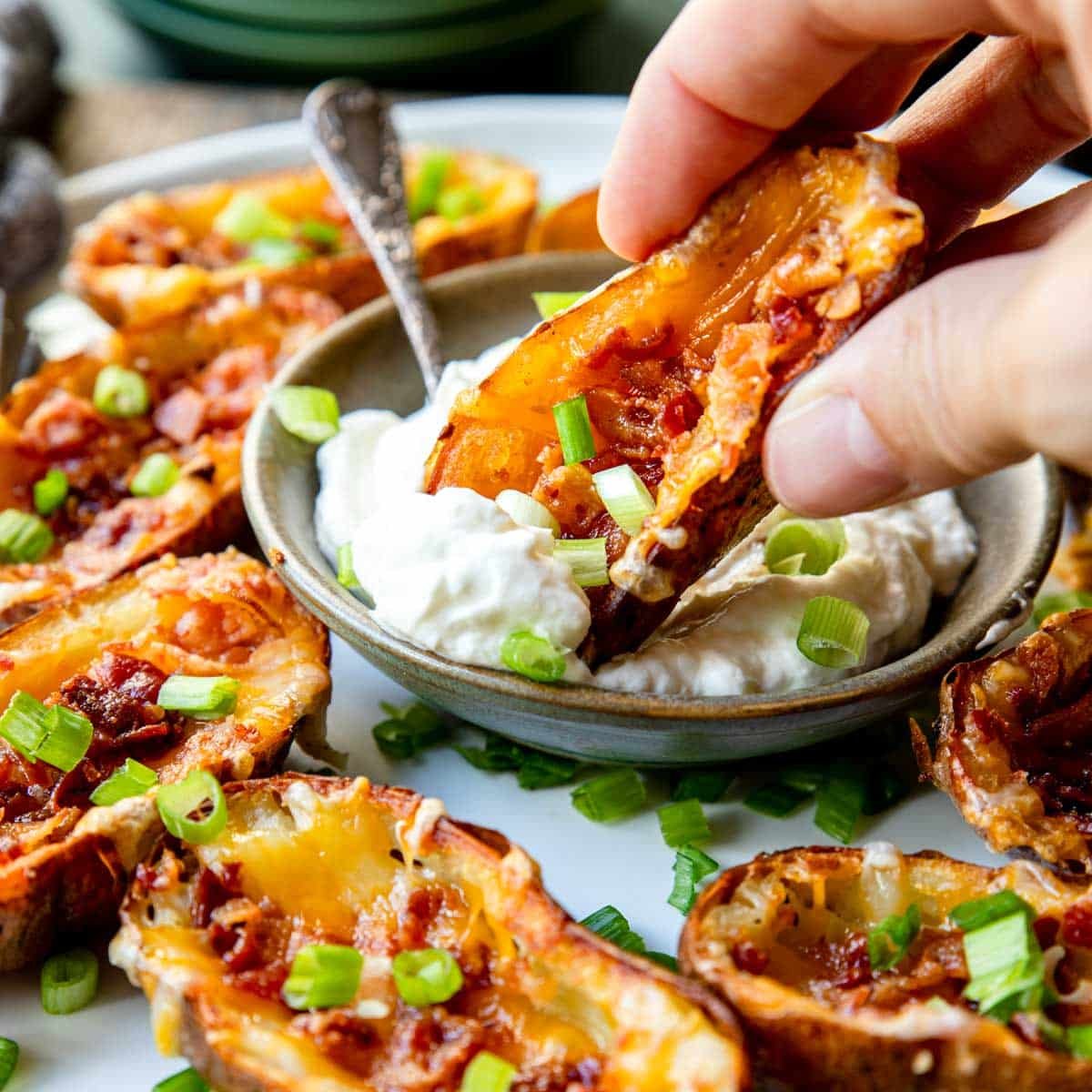 a plate of potato skins with one being dipped in sour cream dip