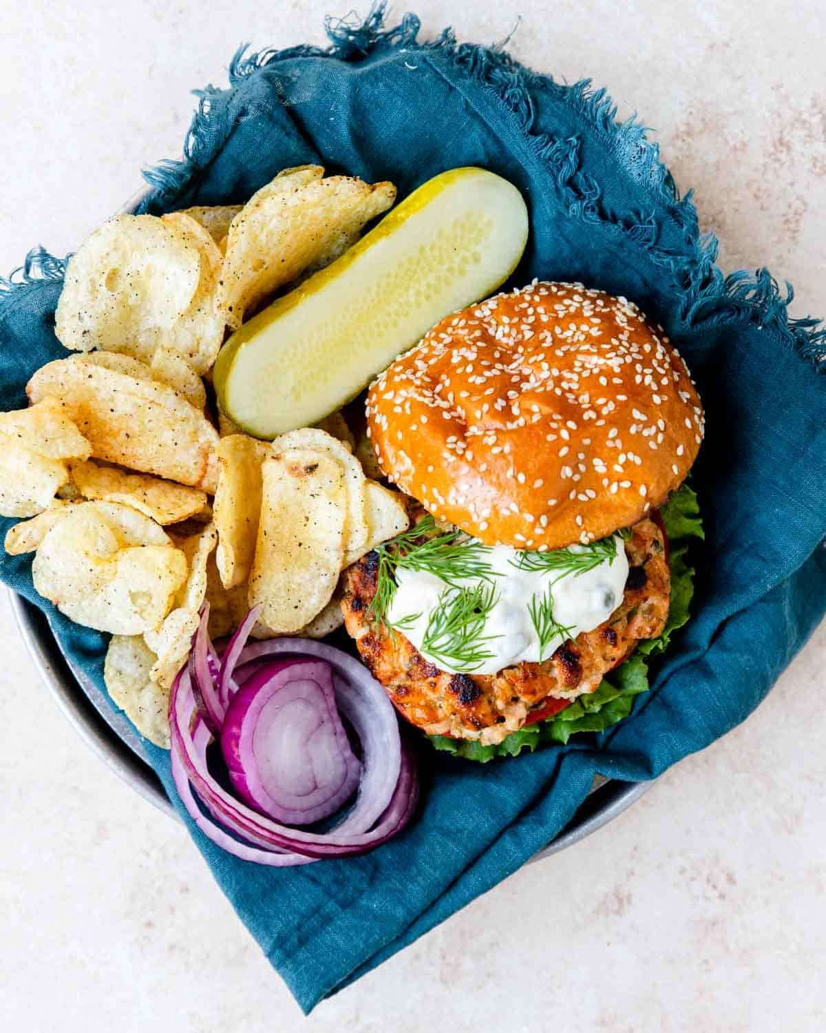 salmon burger with lemon caper mayo on the top with chips and a pickle to the side