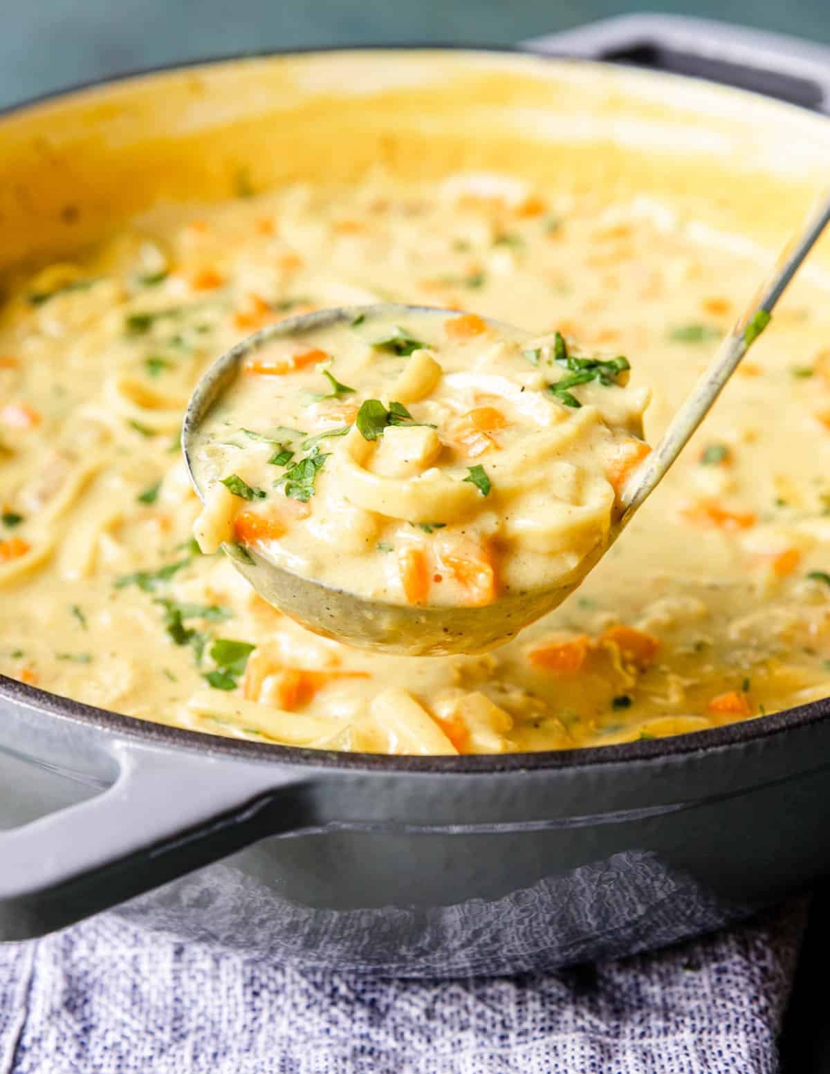 Dutch oven full of creamy chicken noodle soup with a ladle full