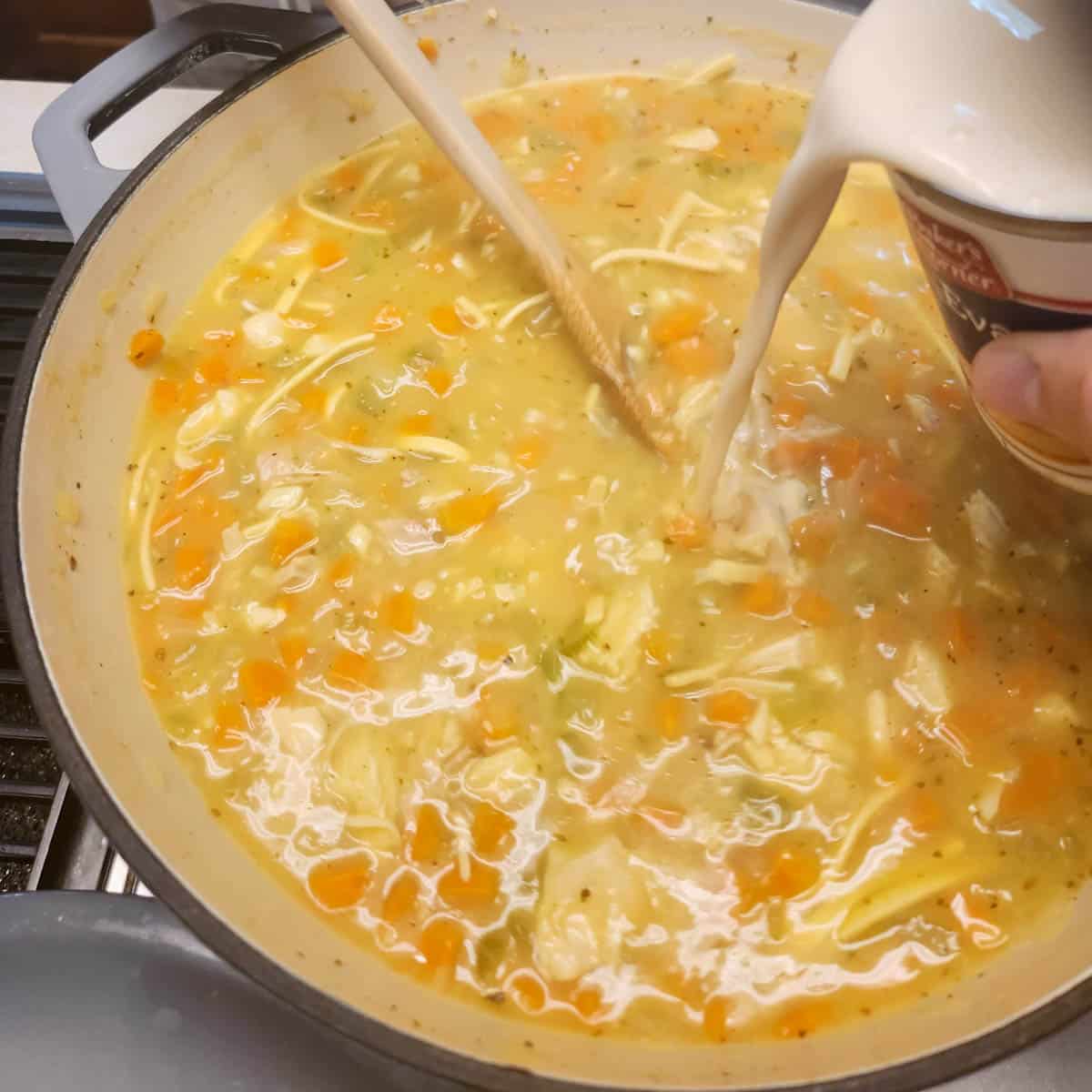 pouring evaporated milk into the creamy chicken noodle soup