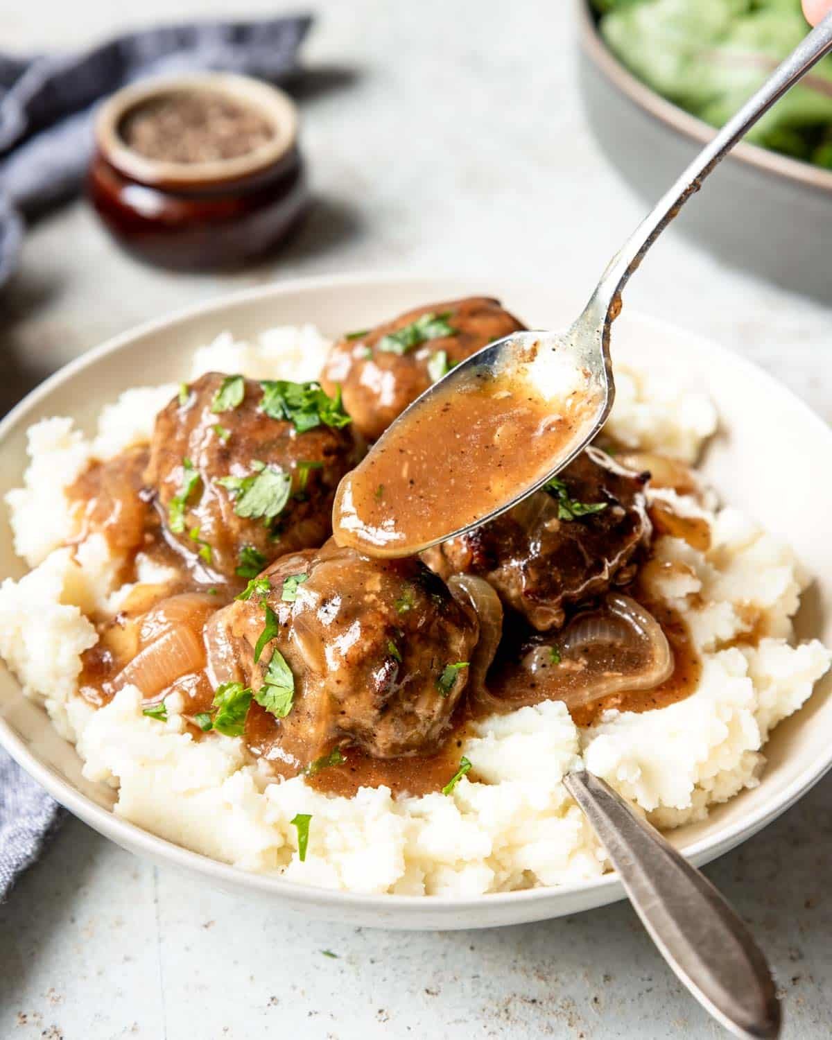 A bowl of mashed potatoes with beef meatballs, with gravy being spooned over top