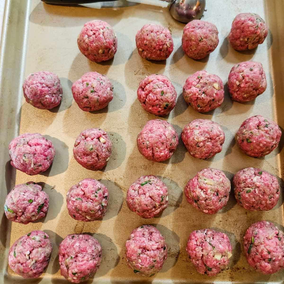 raw beef meatballs on a rimmed baking sheet 