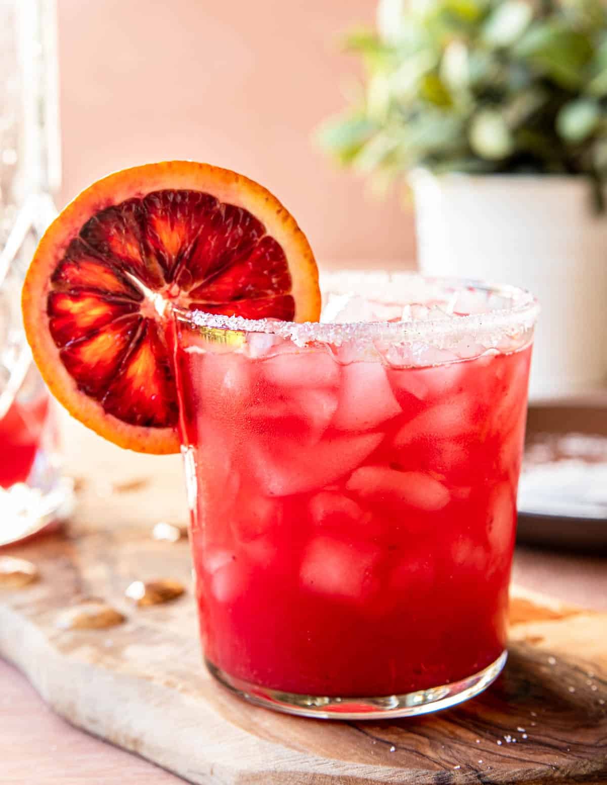 a blood orange margarita in a short glass with salted rim and a blood orange wheel garnish