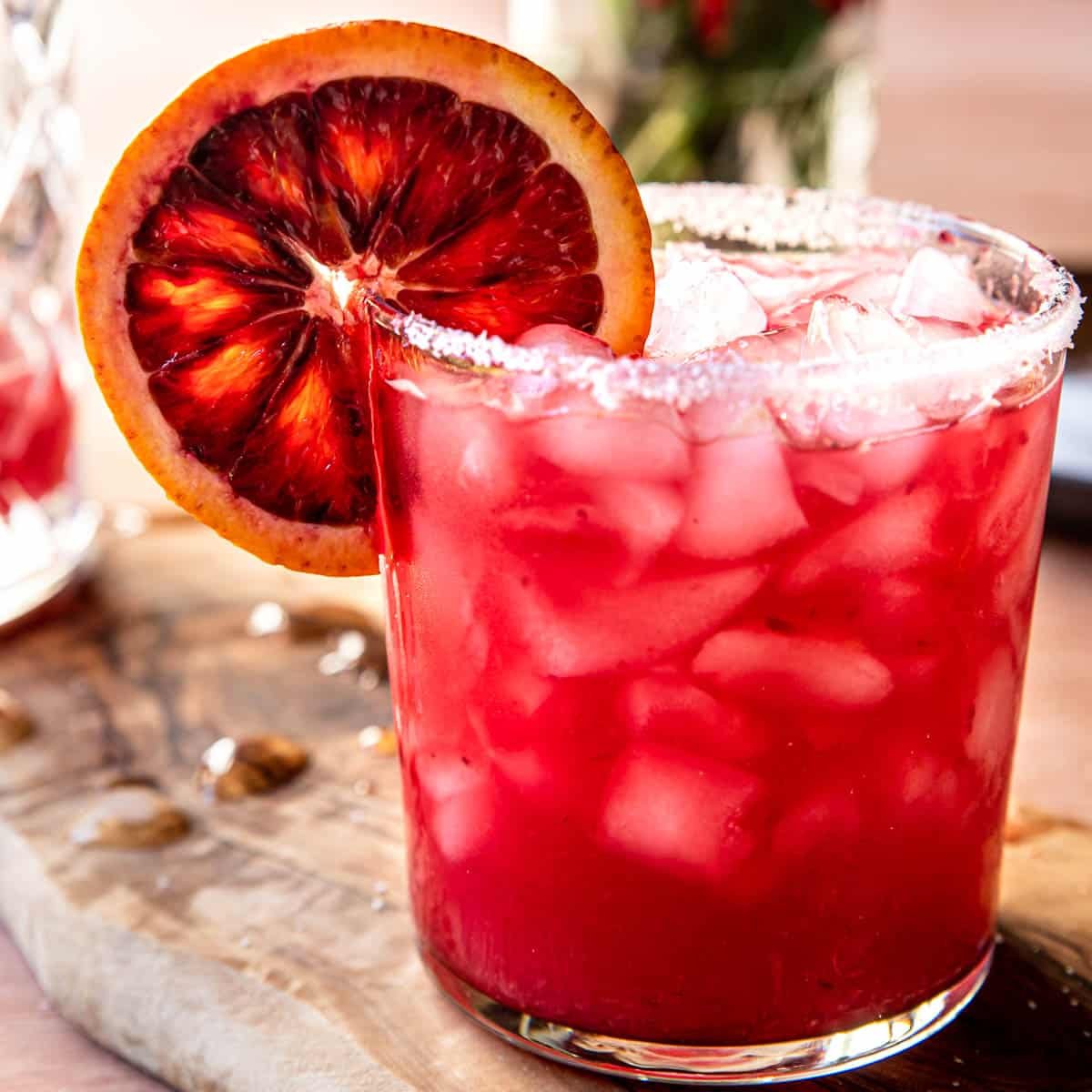 a blood orange margarita in a glass with a salted rim and a blood orange wheel on the side