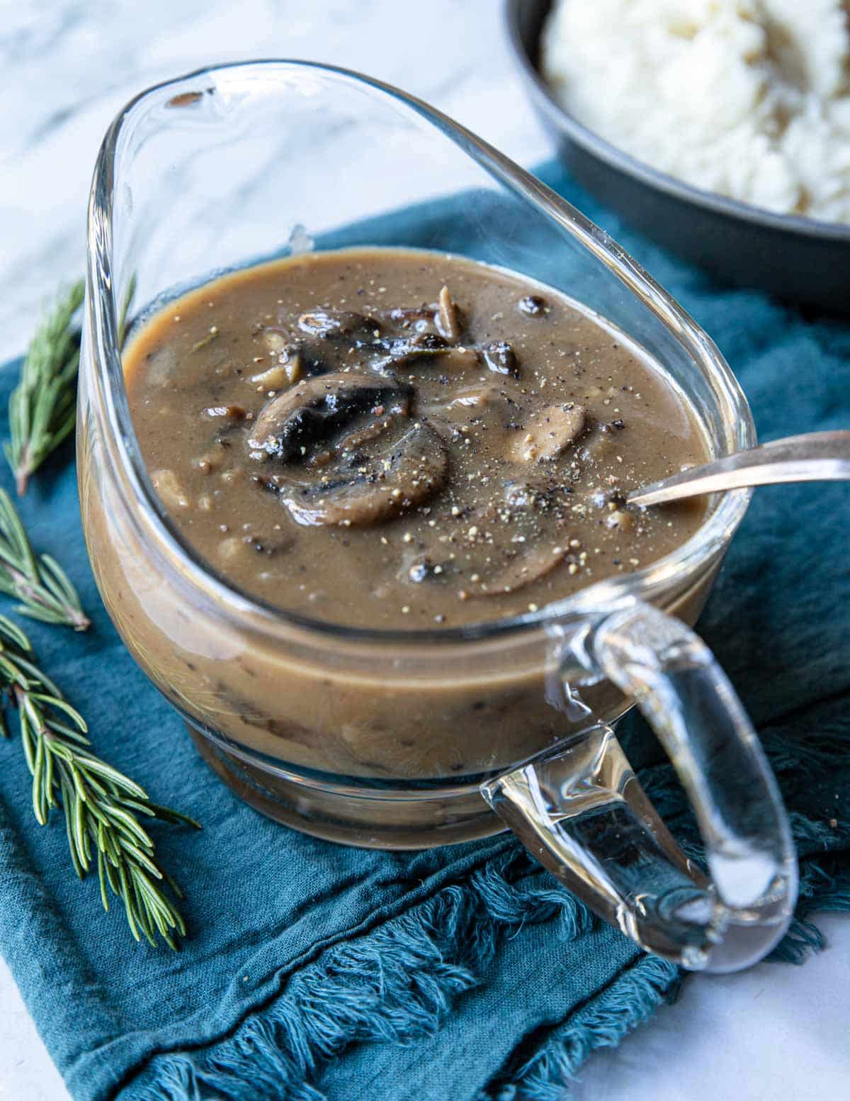 a glass gravy boat with mushroom gravy inside, topped with cracked black pepper