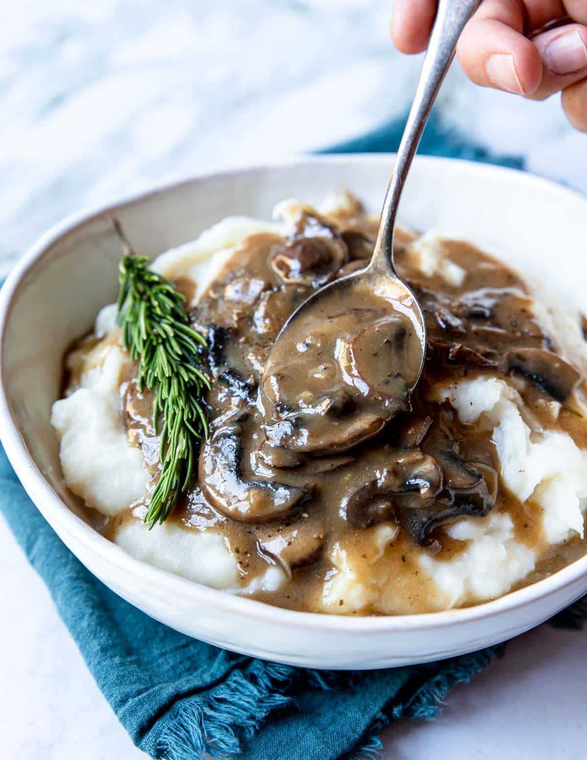 a large bowl of mashed potatoes with mushroom gravy being drizzled over top