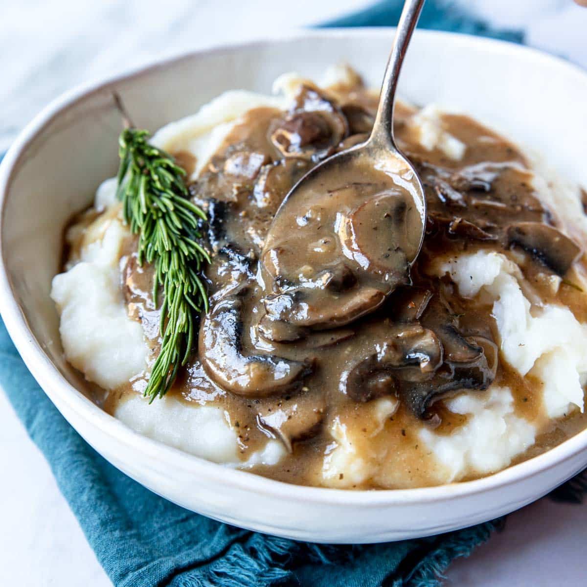 Mushroom gravy being spooned over mashed potatoes