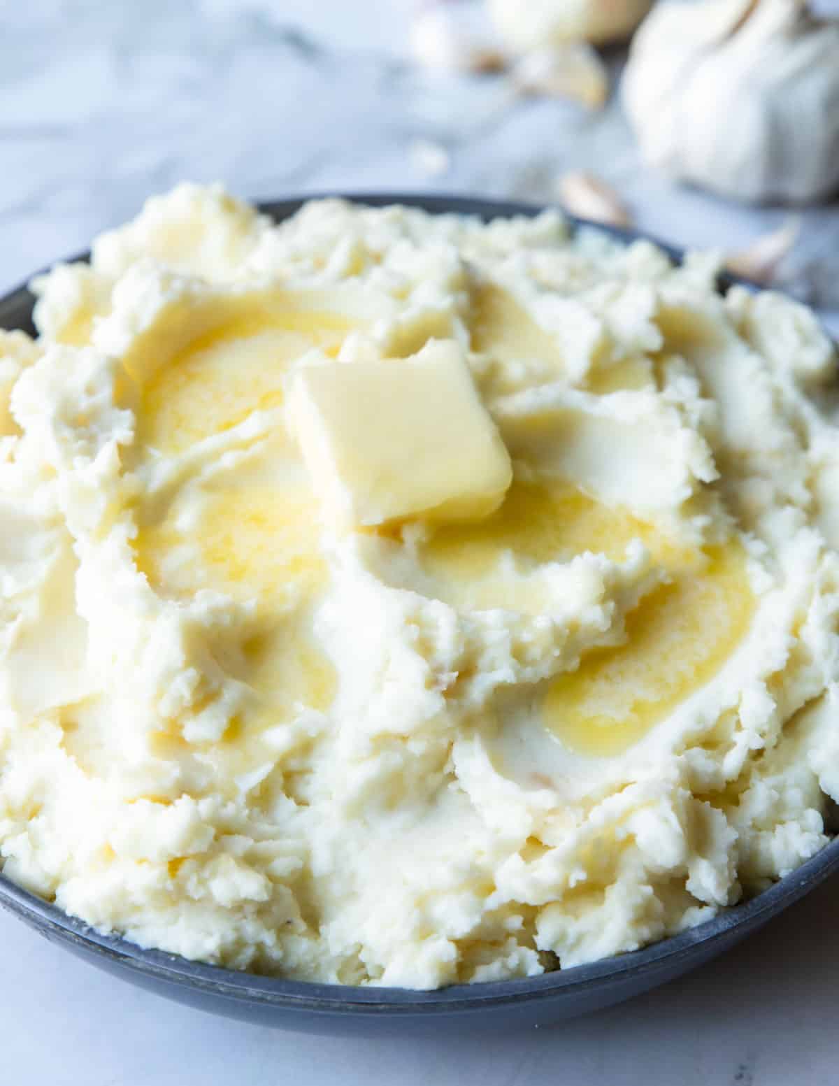 a large bowl of roasted garlic mashed potatoes topped with a large pat of butter