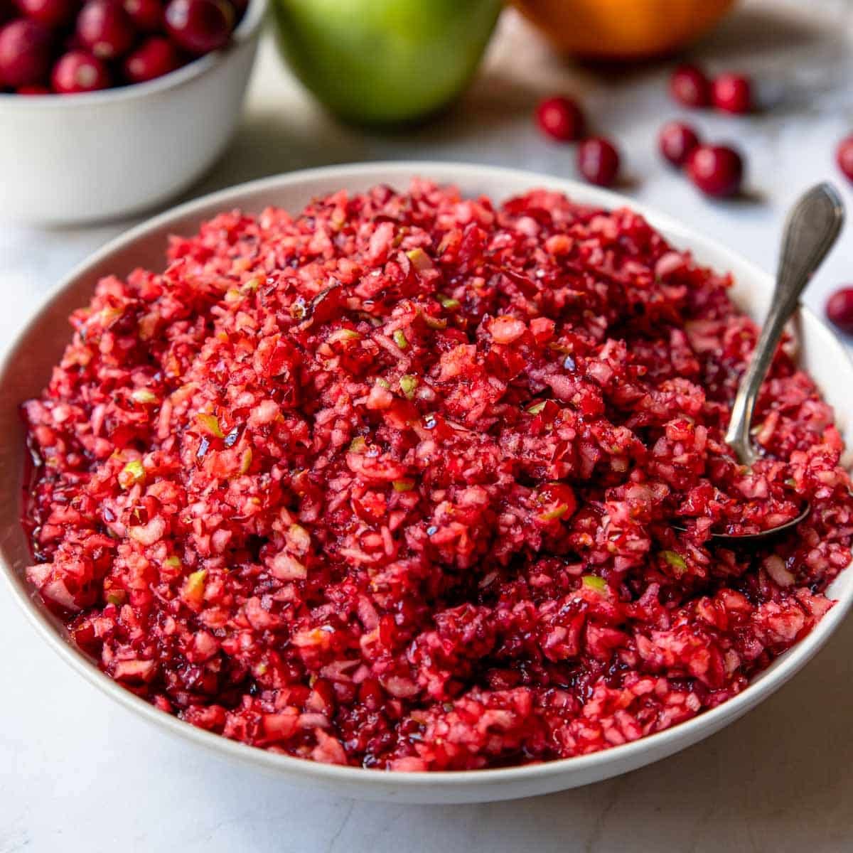 bowl of cranberry relish with a spoon and raw cranberries in the background