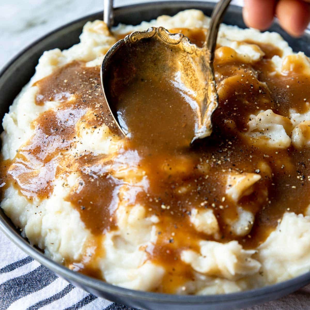 brown gravy being ladled over mashed potatoes
