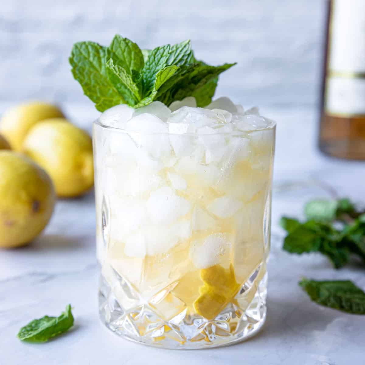 Añejo Tequila Smash in a glass with a lemon in the glass and fresh mint on top