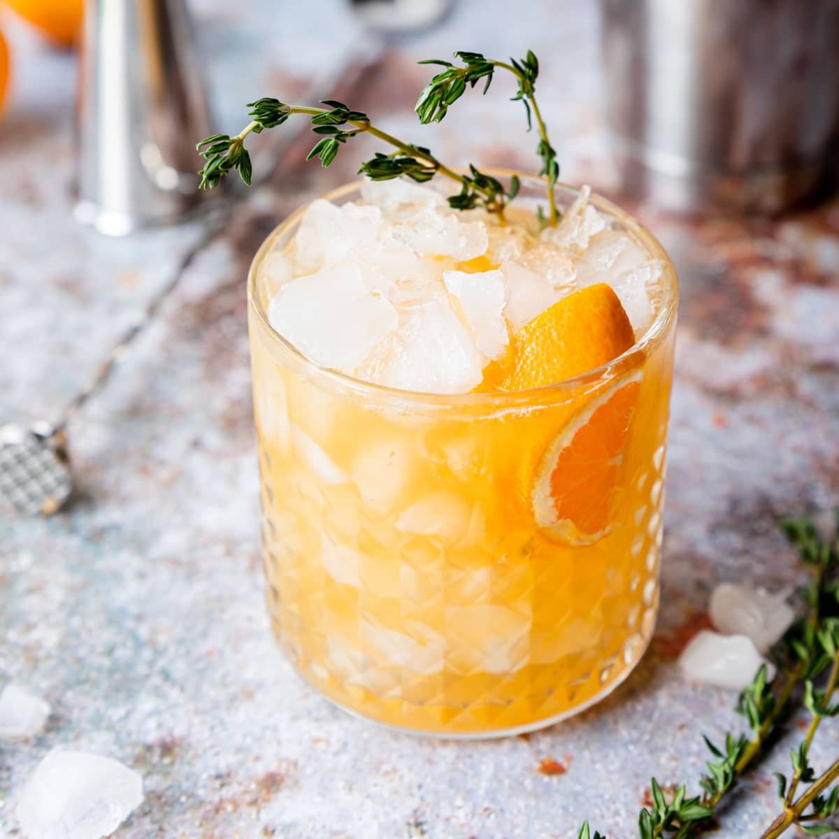 Etched glass filled with an orange smash cocktail garnished with fresh thyme