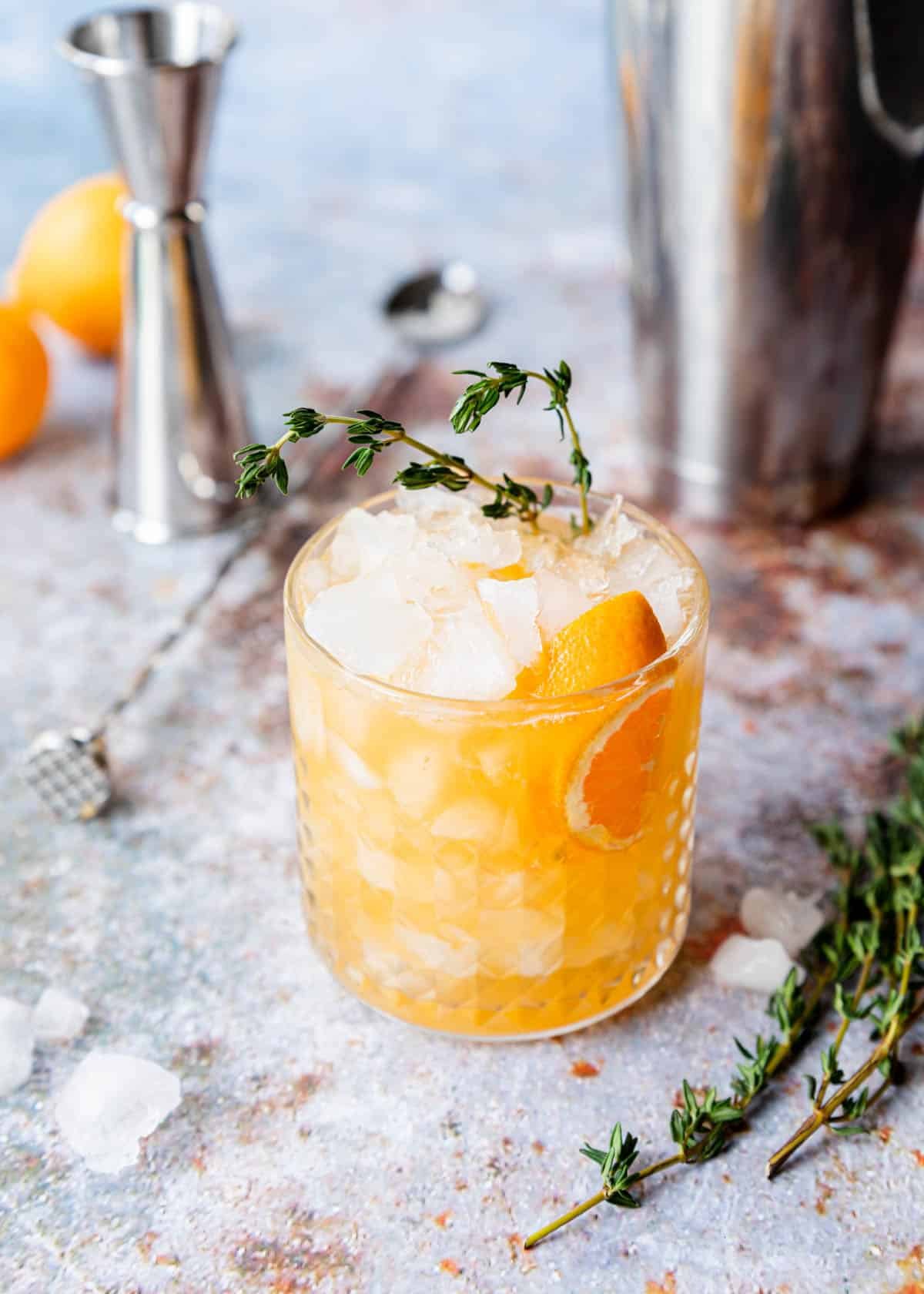 Tequila Smash with orange and thyme on a table with a cocktail muddler and shaker