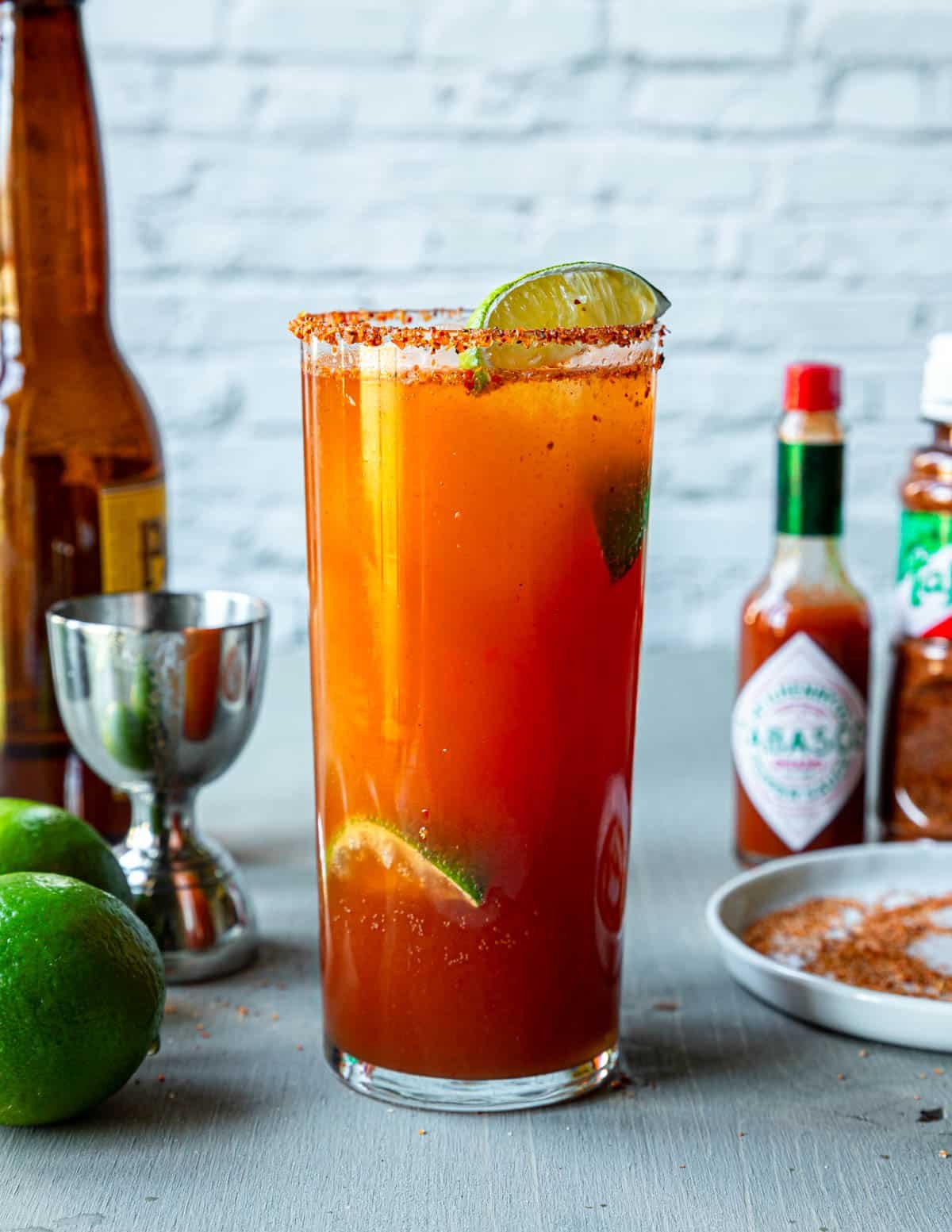 A tall glass of Michelada with a Tajin rim and lime wedges 