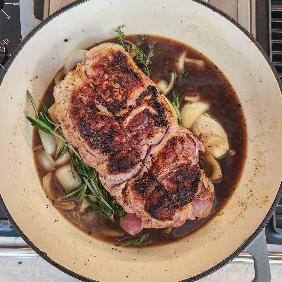 pork shoulder roast with onions, garlic, broth and herbs in a Dutch Oven