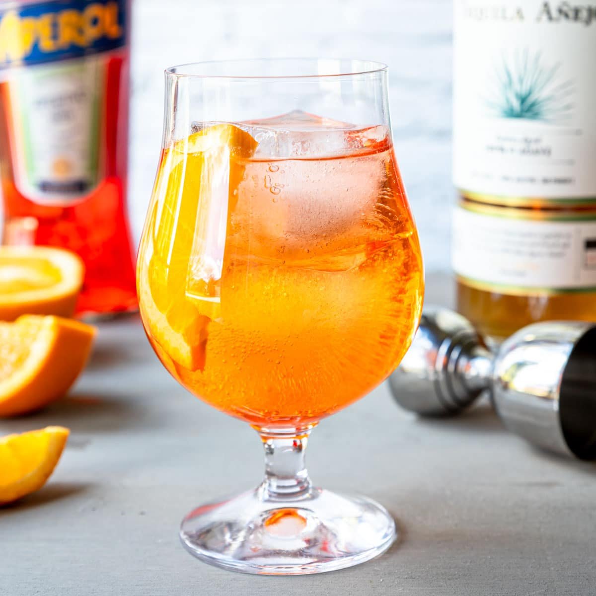 Aperol and Tequila in a glass with ice and topped with soda water, garnished with an orange