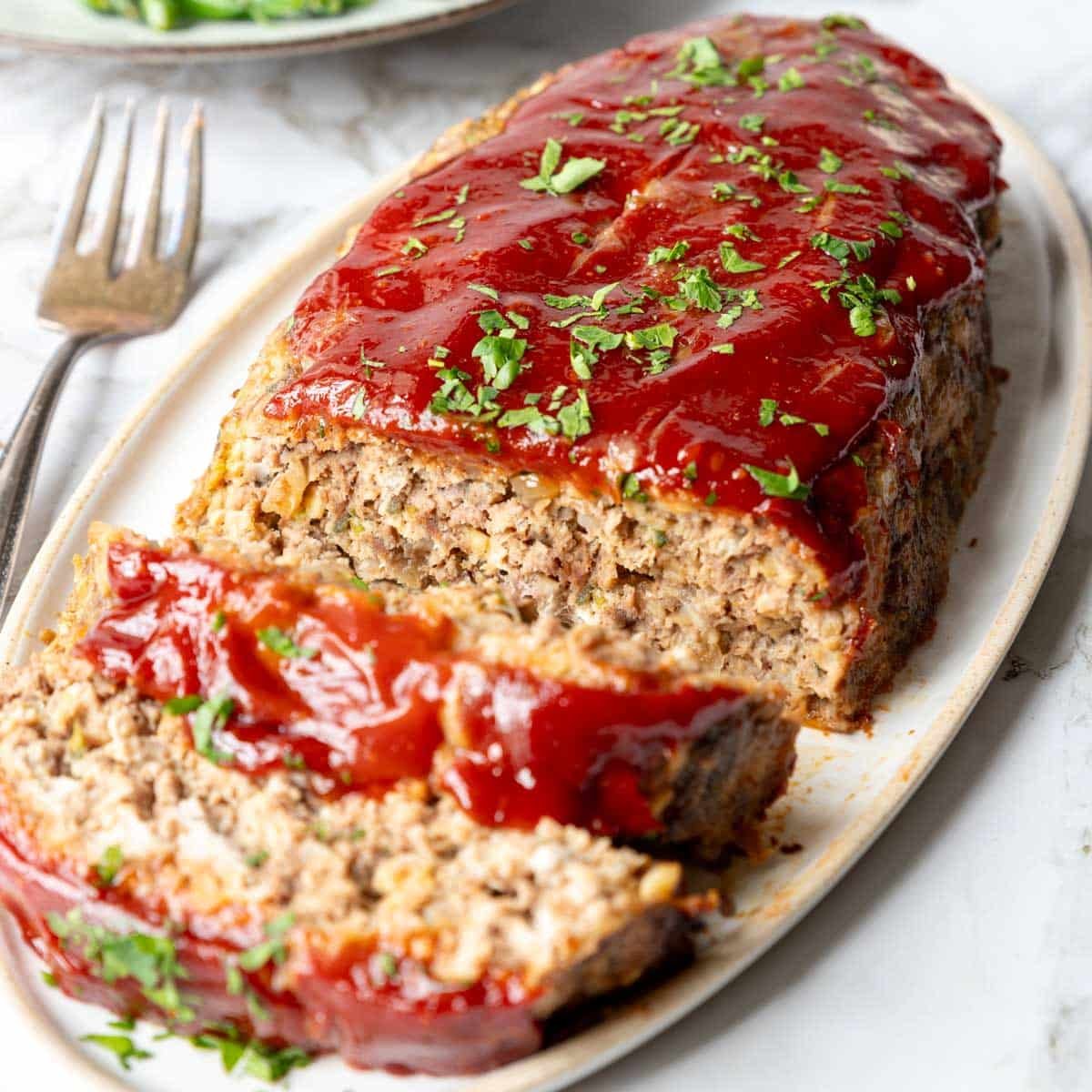 meatloaf with a ketchup topping, on a platter with two slices cut