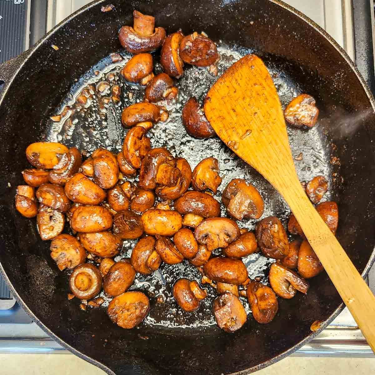 Steakhouse mushrooms in a cast iron skillet with a wooden spoon