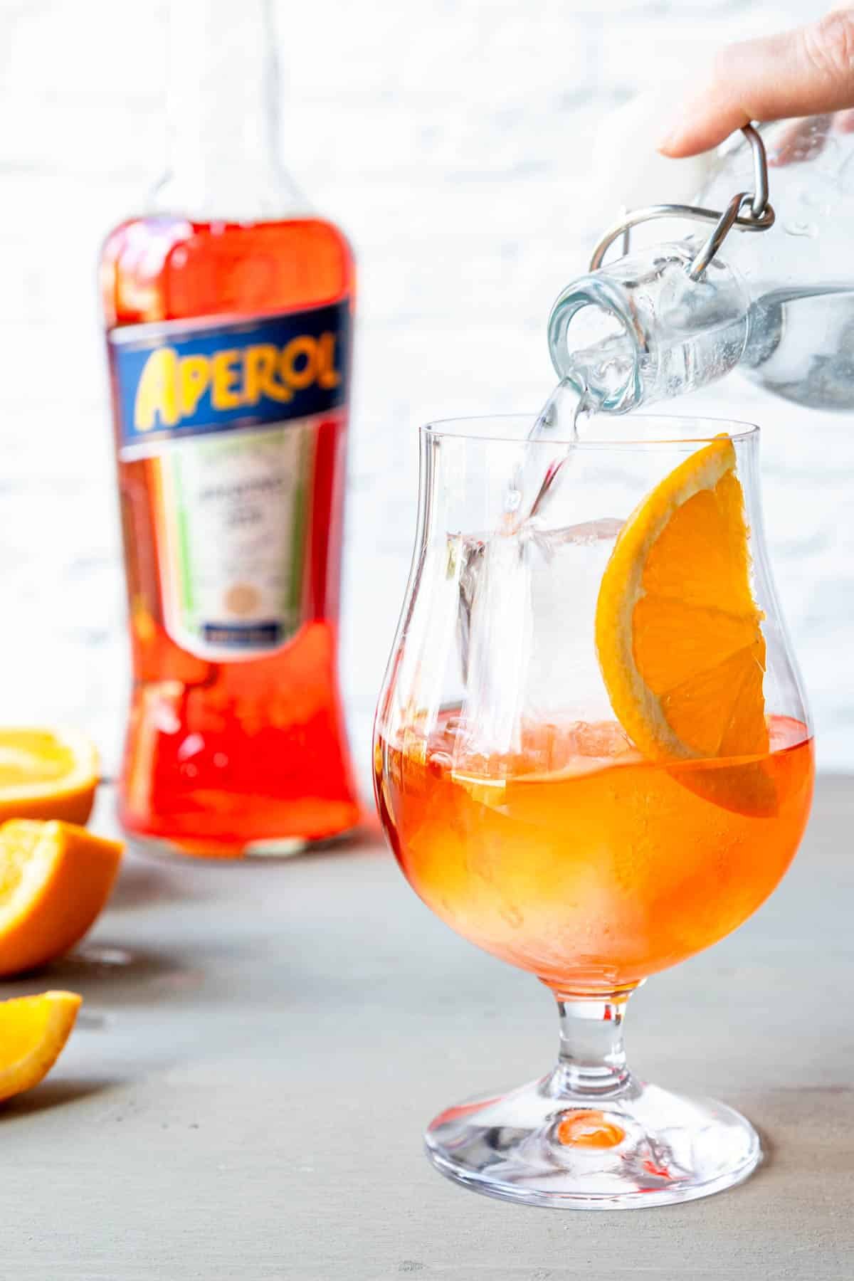 pouring soda water into aperol and tequila