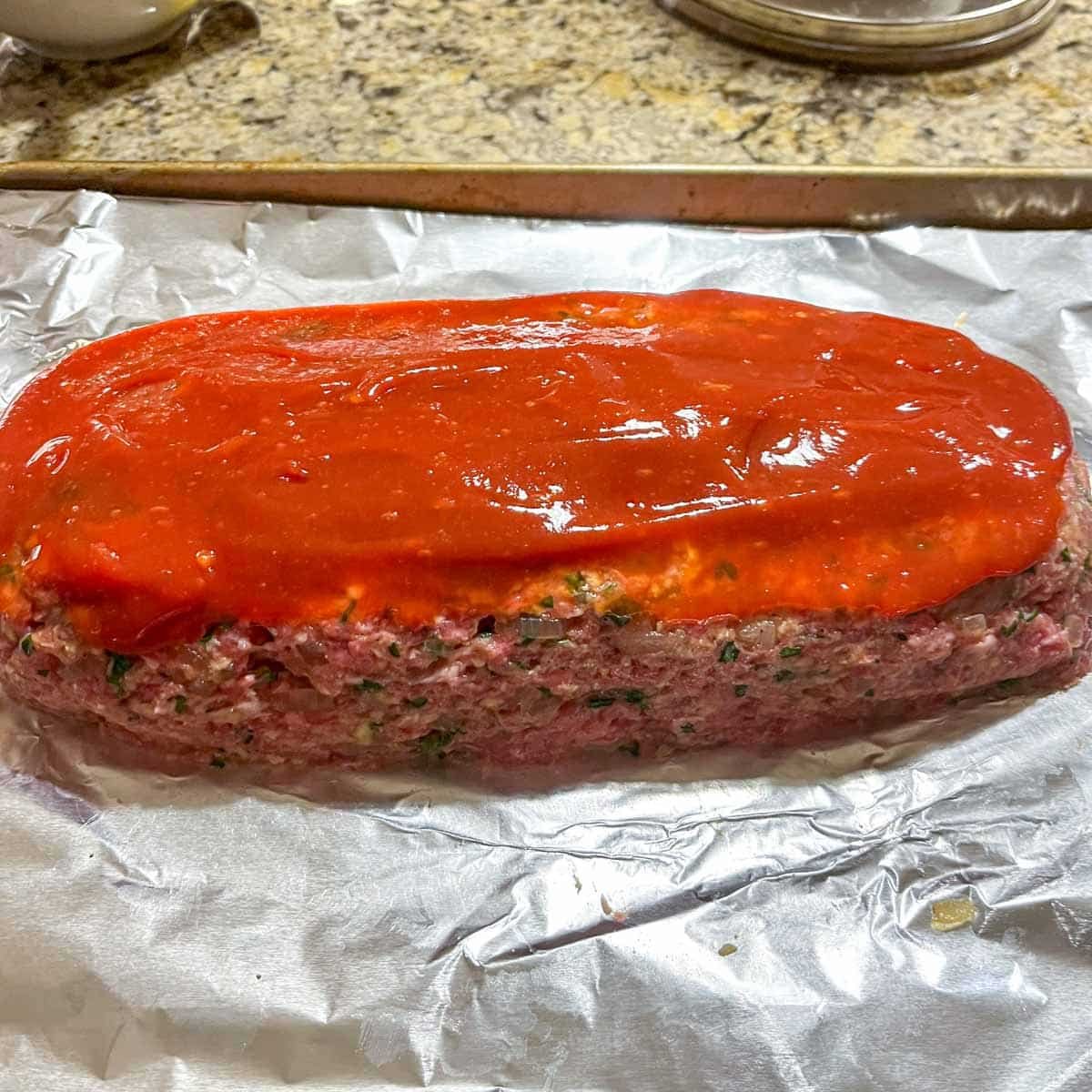 raw meatloaf formed with ketchup topping spread on