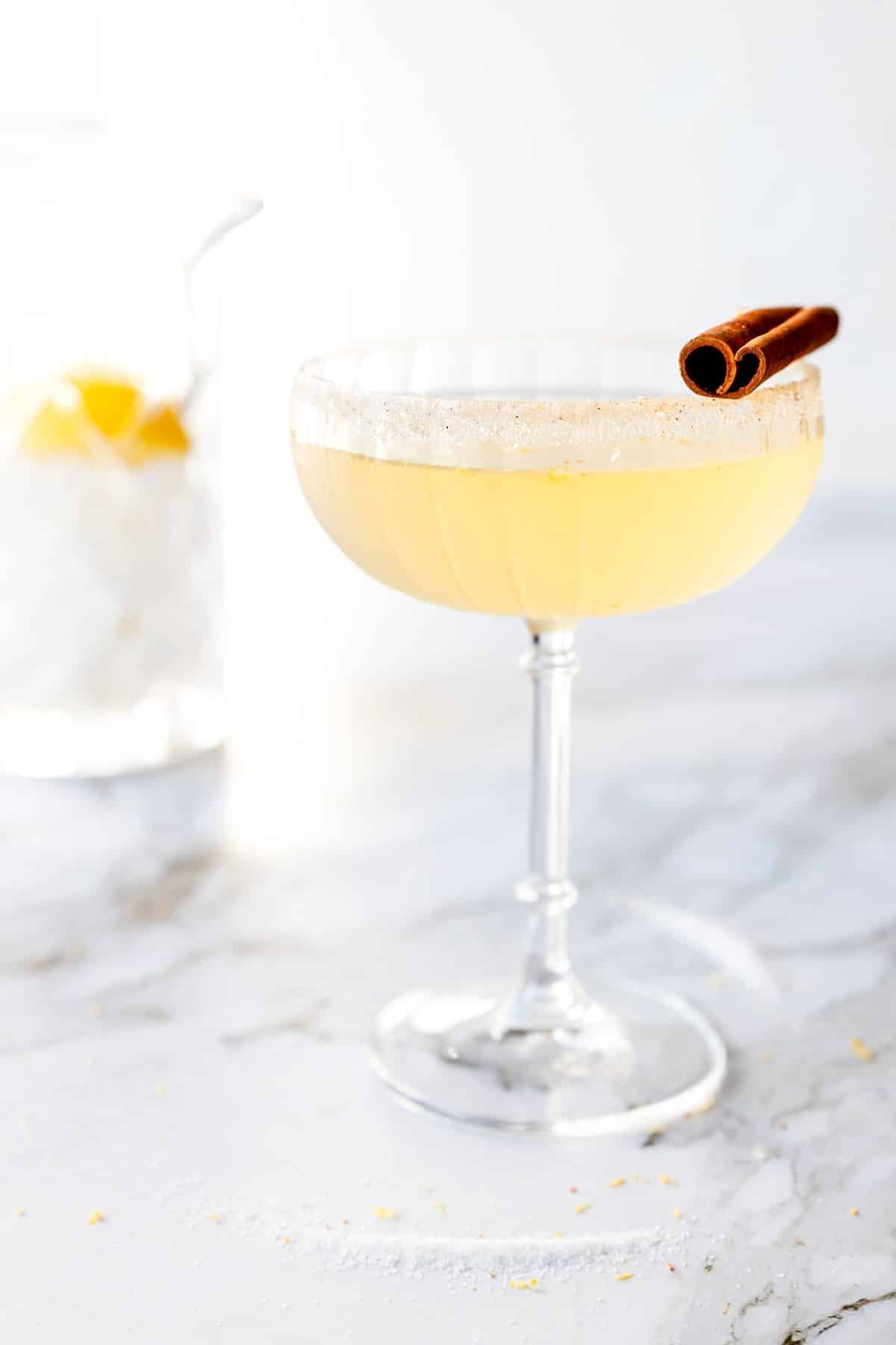 Coupe glass with a cinnamon sugar rim with a cinnamon stick and a cinnamon tequila lemon drop cocktail