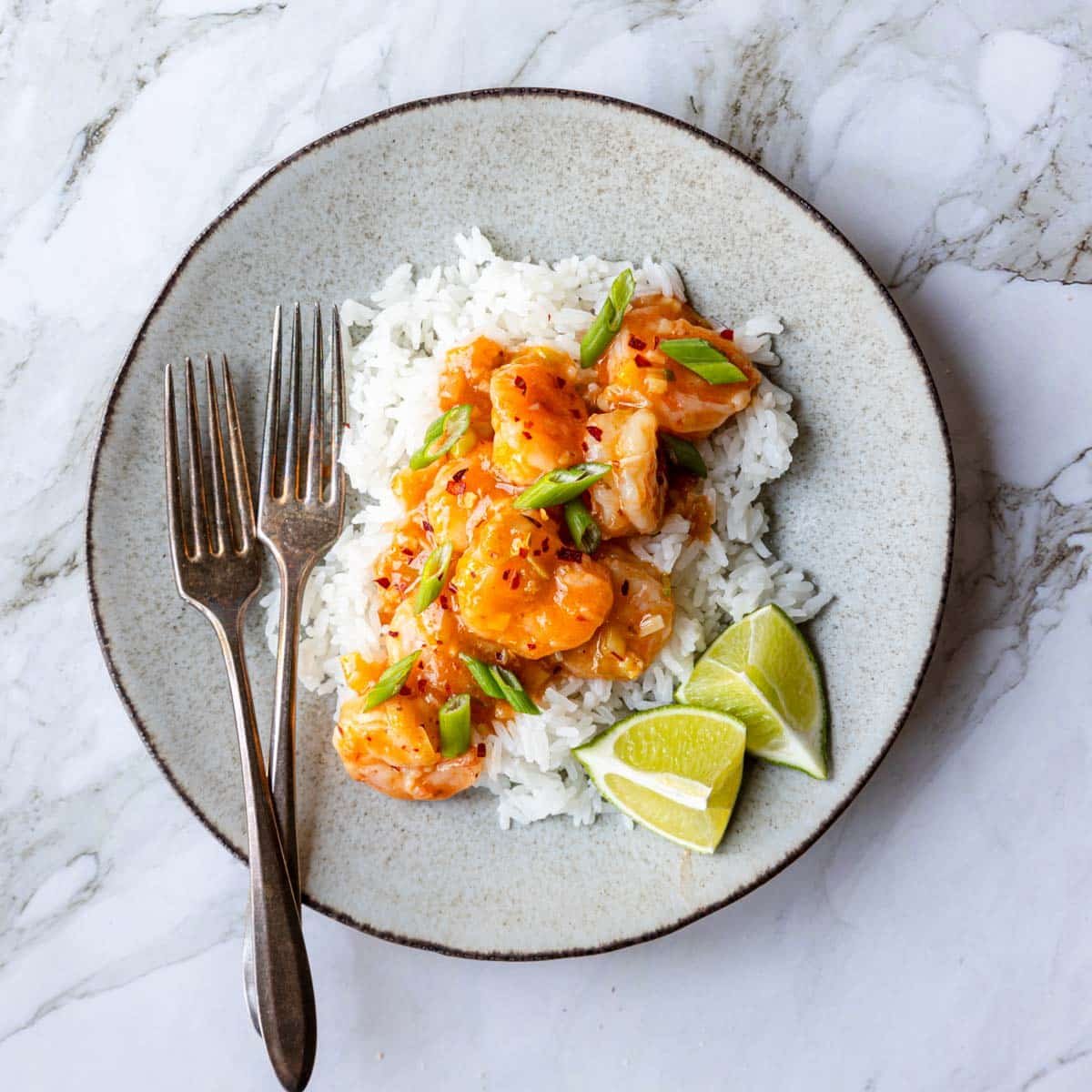 a plate of rice topped with ginger garlic shrimp and lime wedges on the side