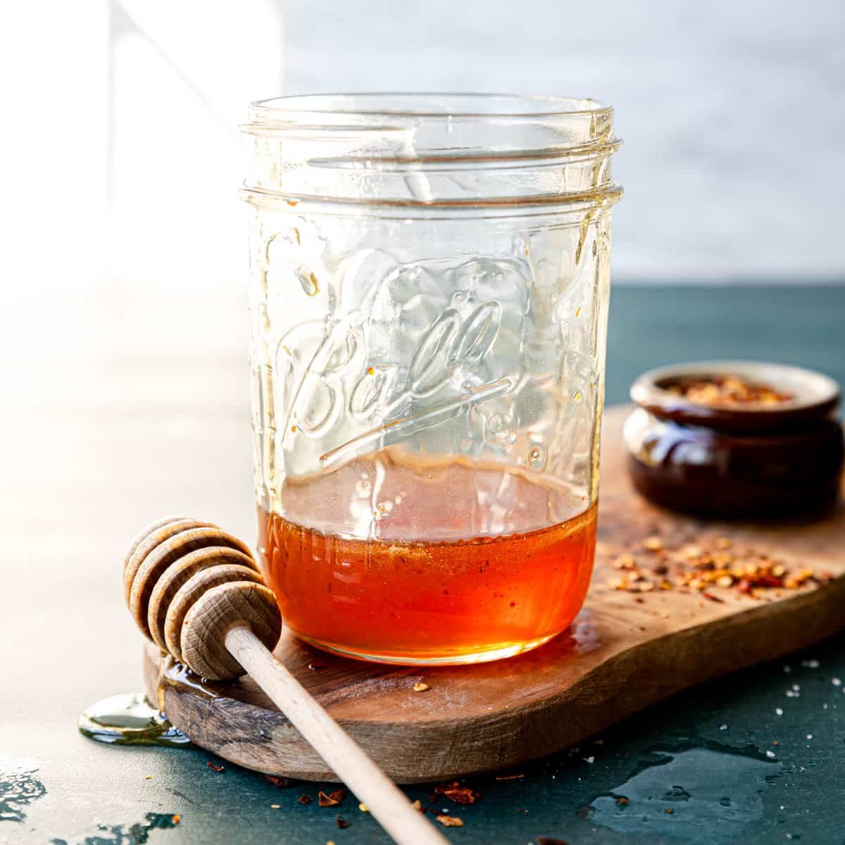 hot honey in a mason jar with a honey stick to the side and red pepper flakes on the cutting board