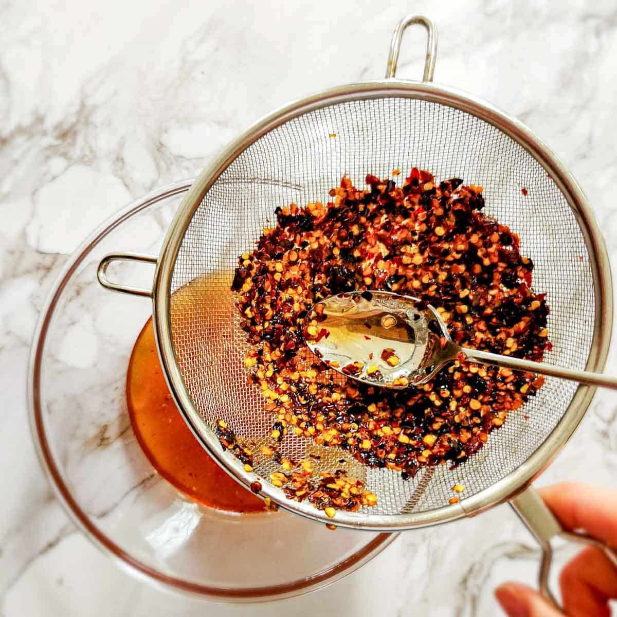 red pepper flakes and honey in a fine mesh sieve over a bowl