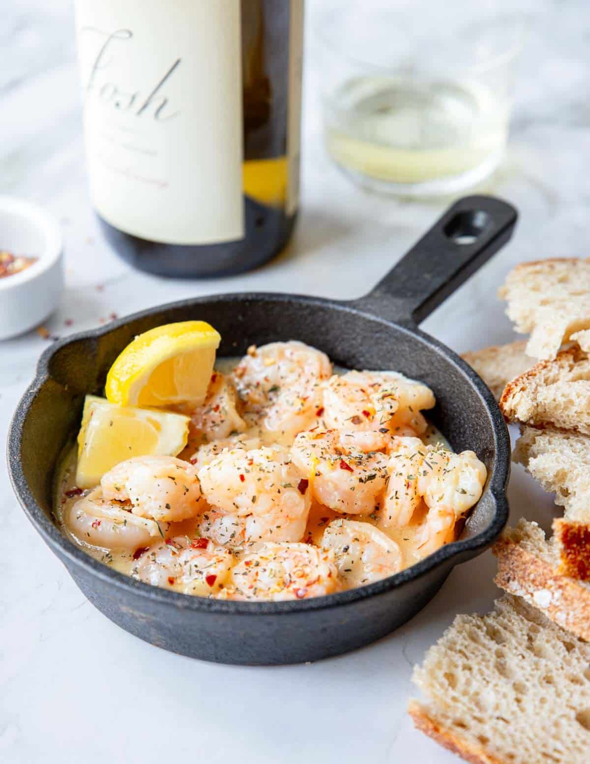 a small skillet with garlic butter shrimp and a bottle of white wine in the background 