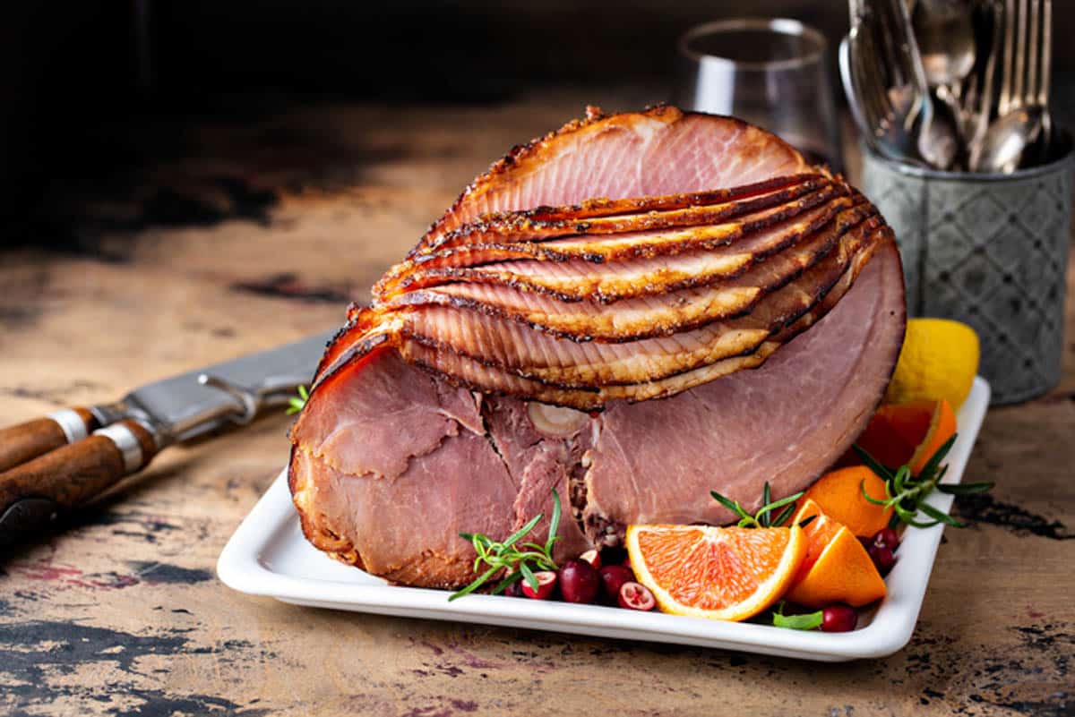 a spiral ham on a table, garnished with oranges and rosemary