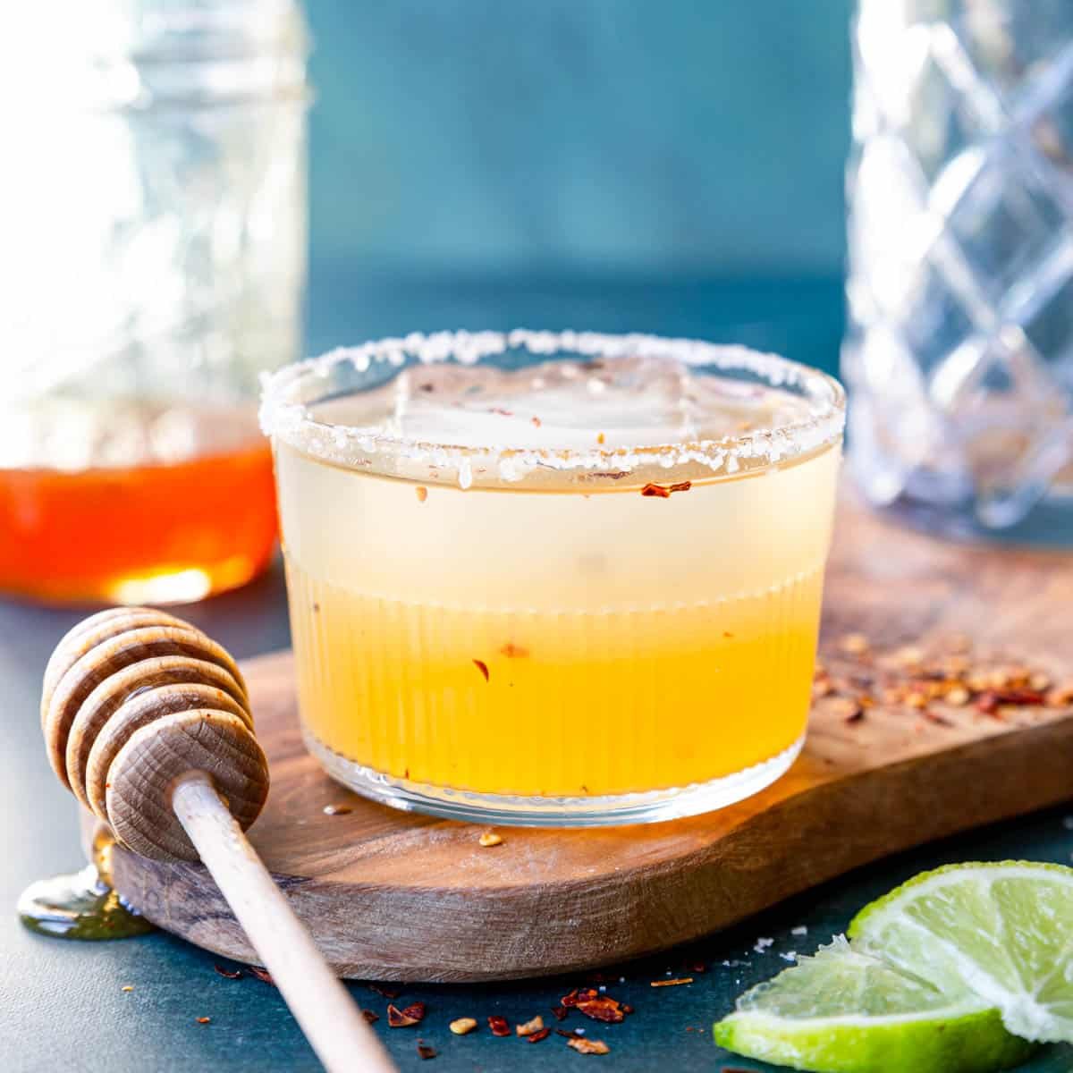 hot honey margarita in a short glass with a salt rim and red pepper flakes on the tables with hot honey in a jar in the background