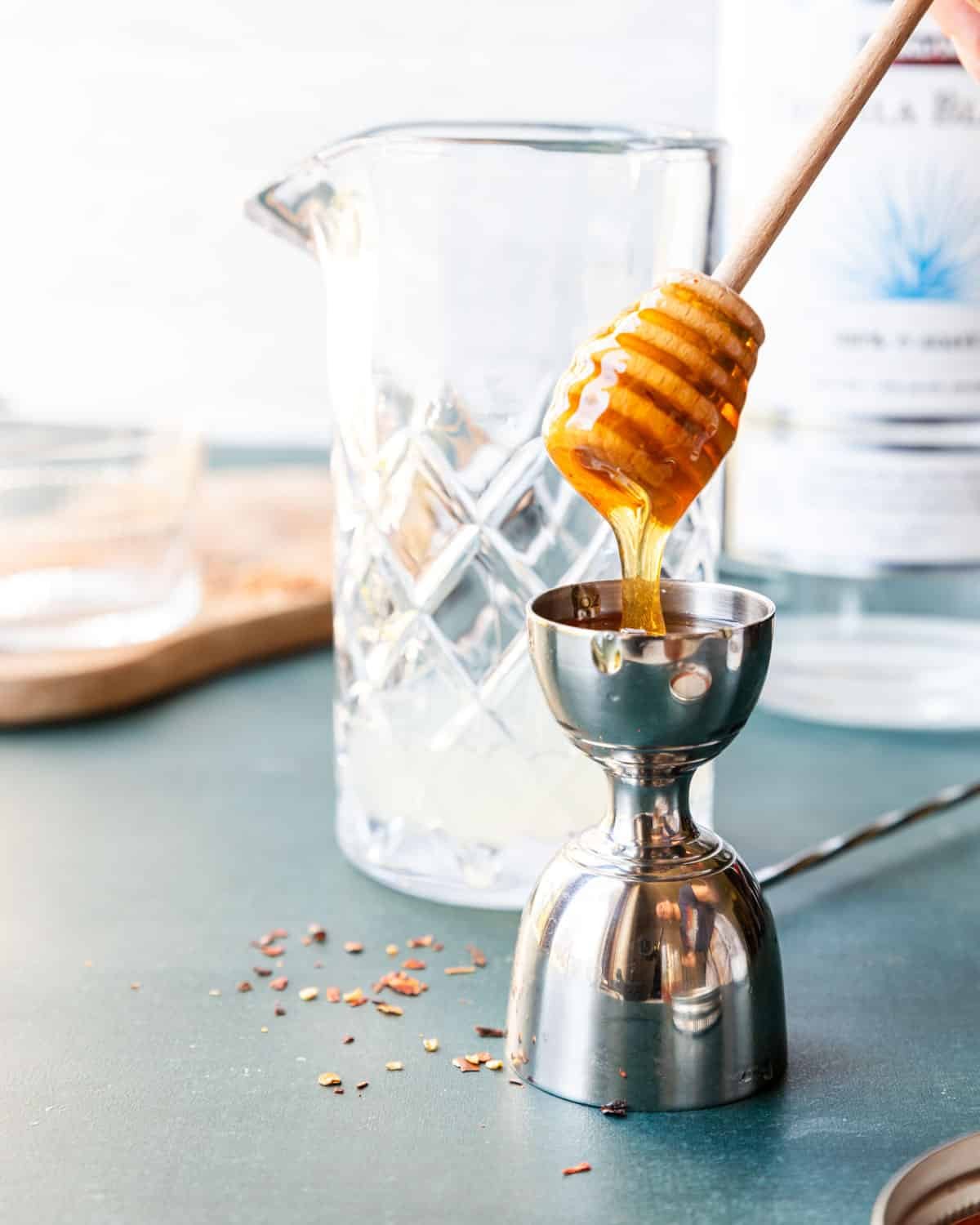 a honey comb spoon drizzling hot honey into a cocktail jigger