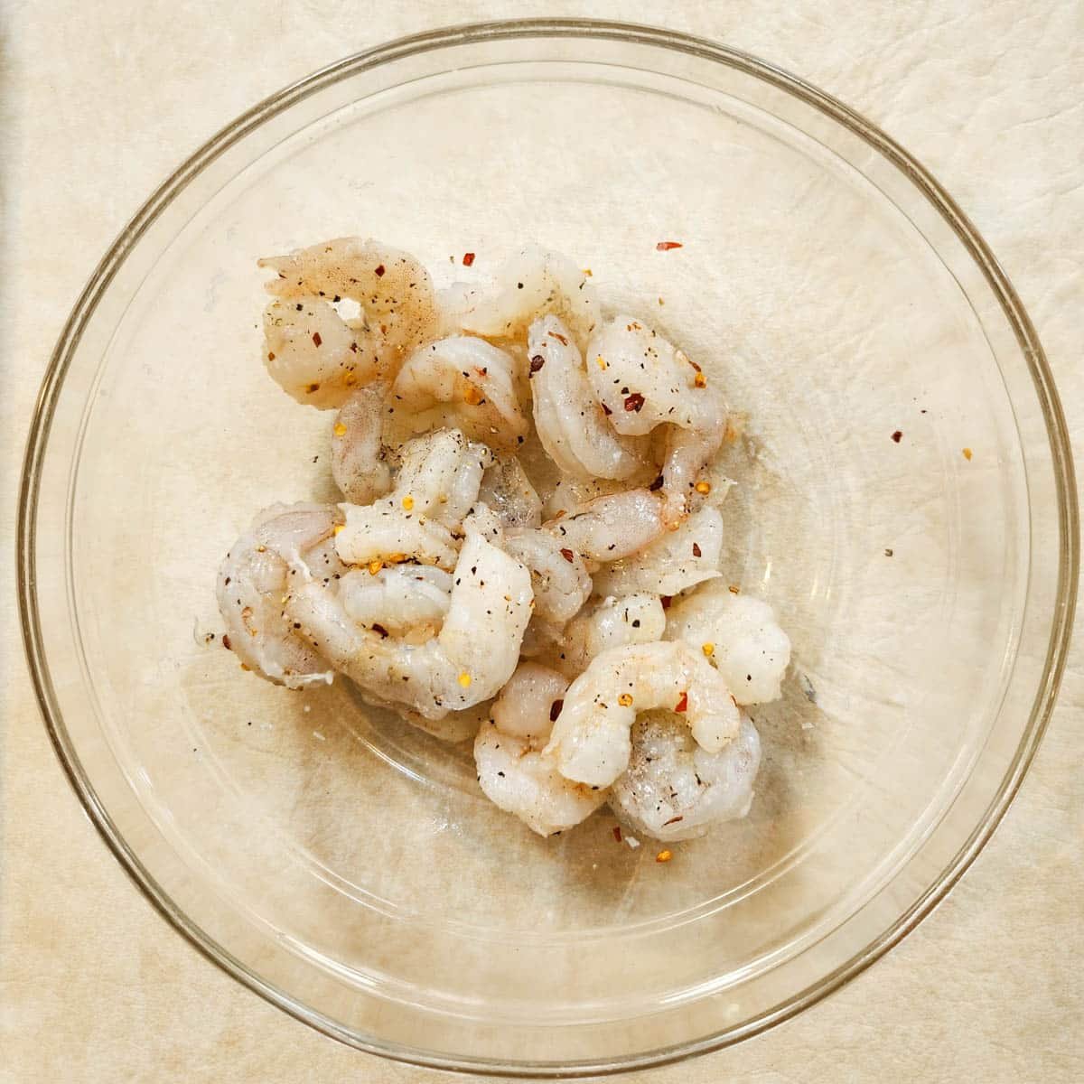 shrimp in a bowl with kosher salt, black pepper and red pepper flakes