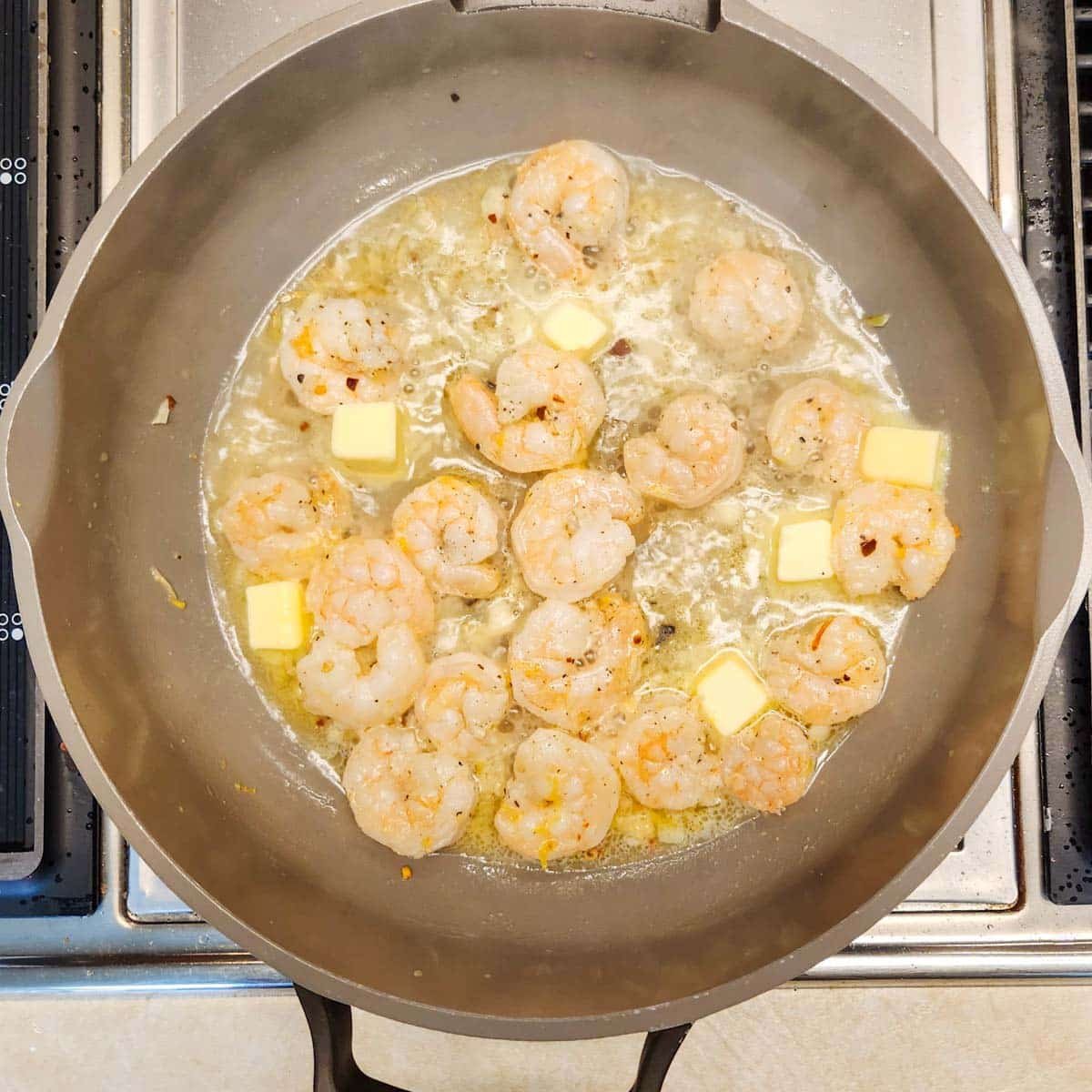 a skillet with shrimp, white wine, garlic and extra butter melting around the pan