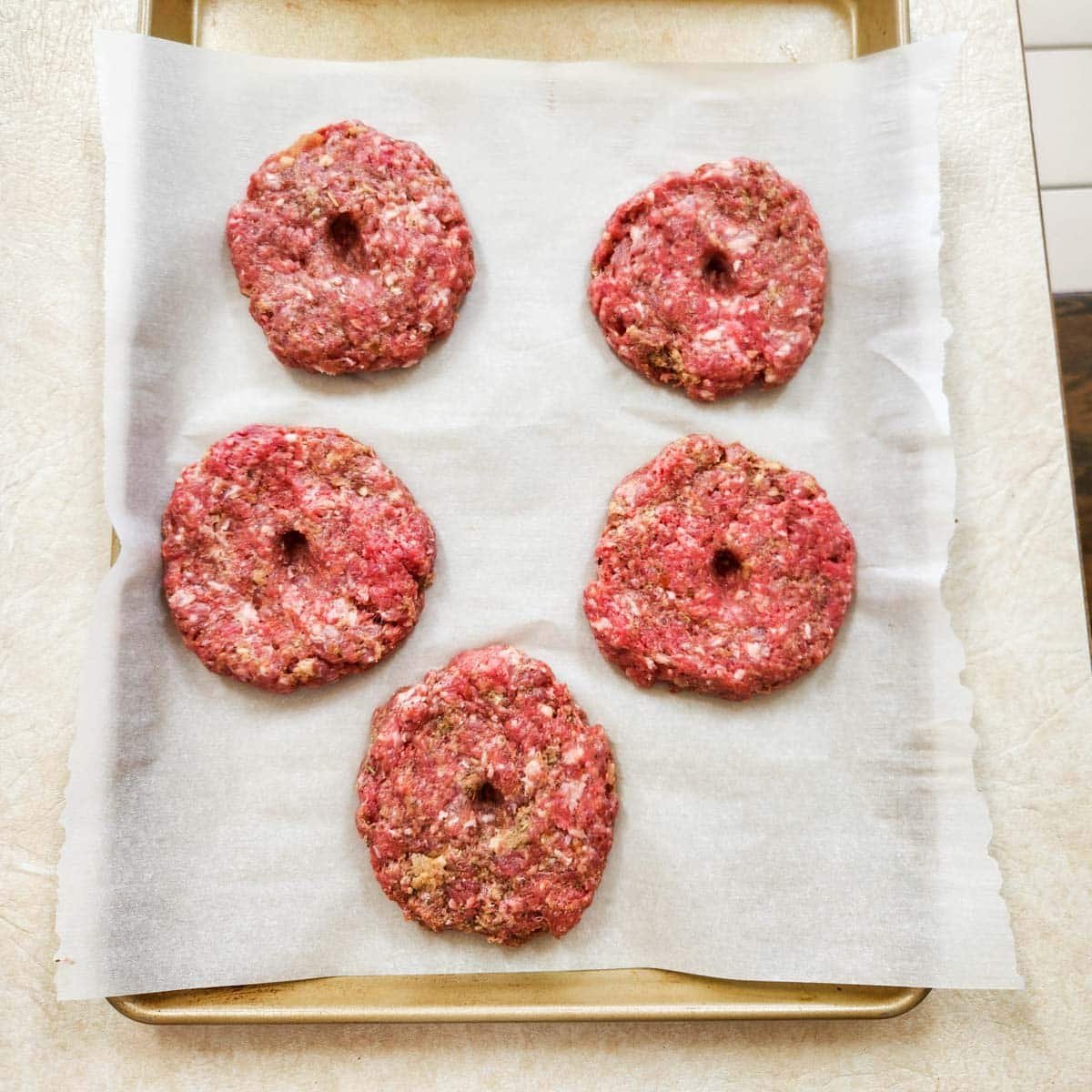raw pizza burger patties on a rimmed baking sheet with parchment