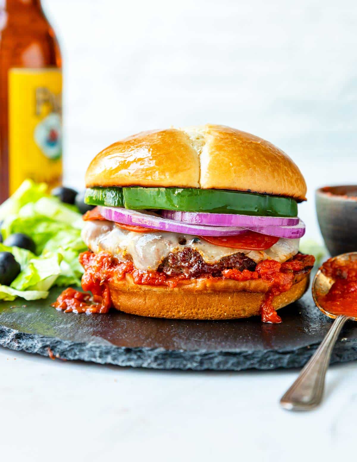 a pizza burger topped with cheese, onion, pepperoni and green pepper, on a black plate with 