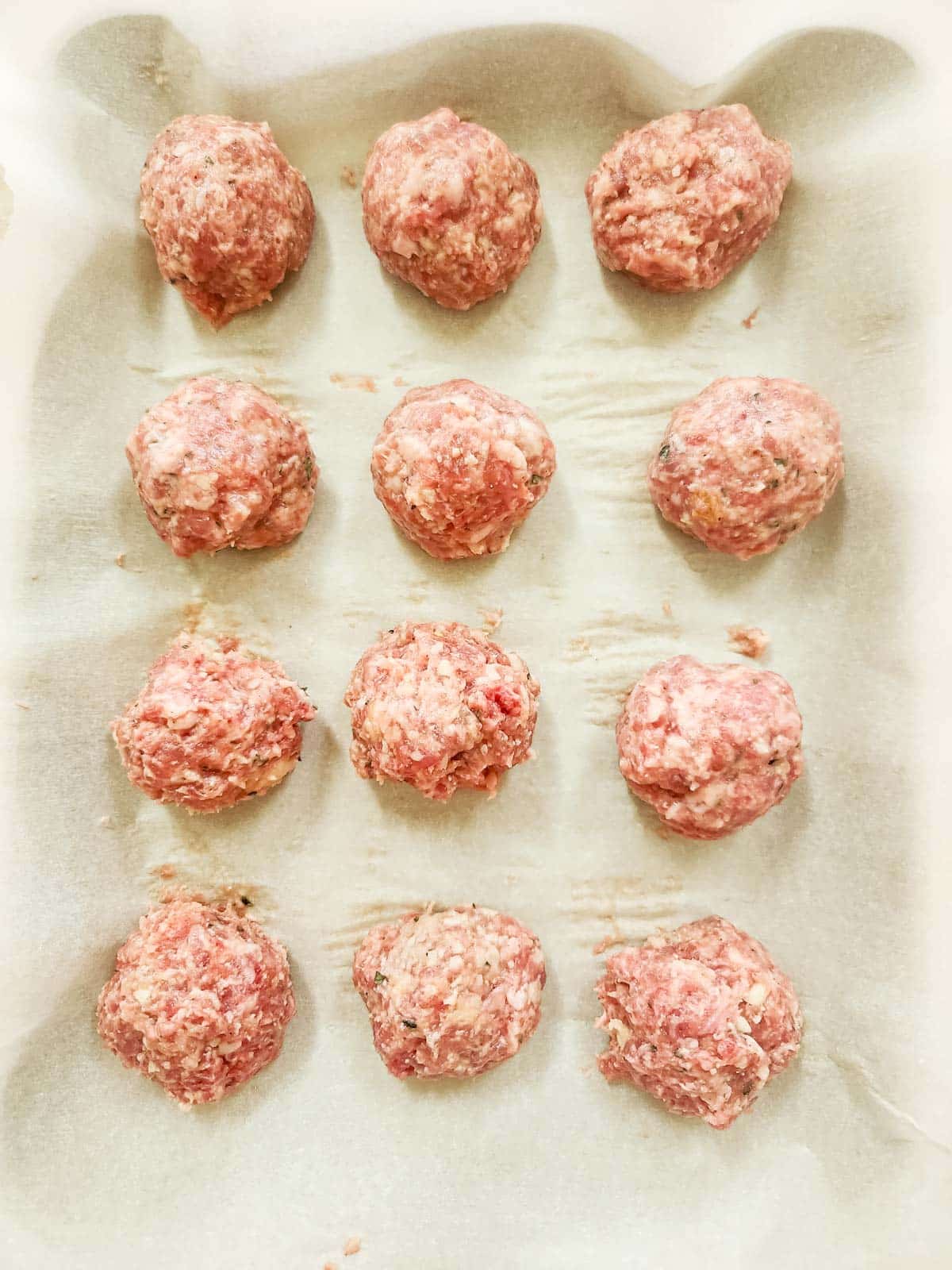 a parchment lined baking sheet full of raw Italian Sausage Meatballs ready for the oven