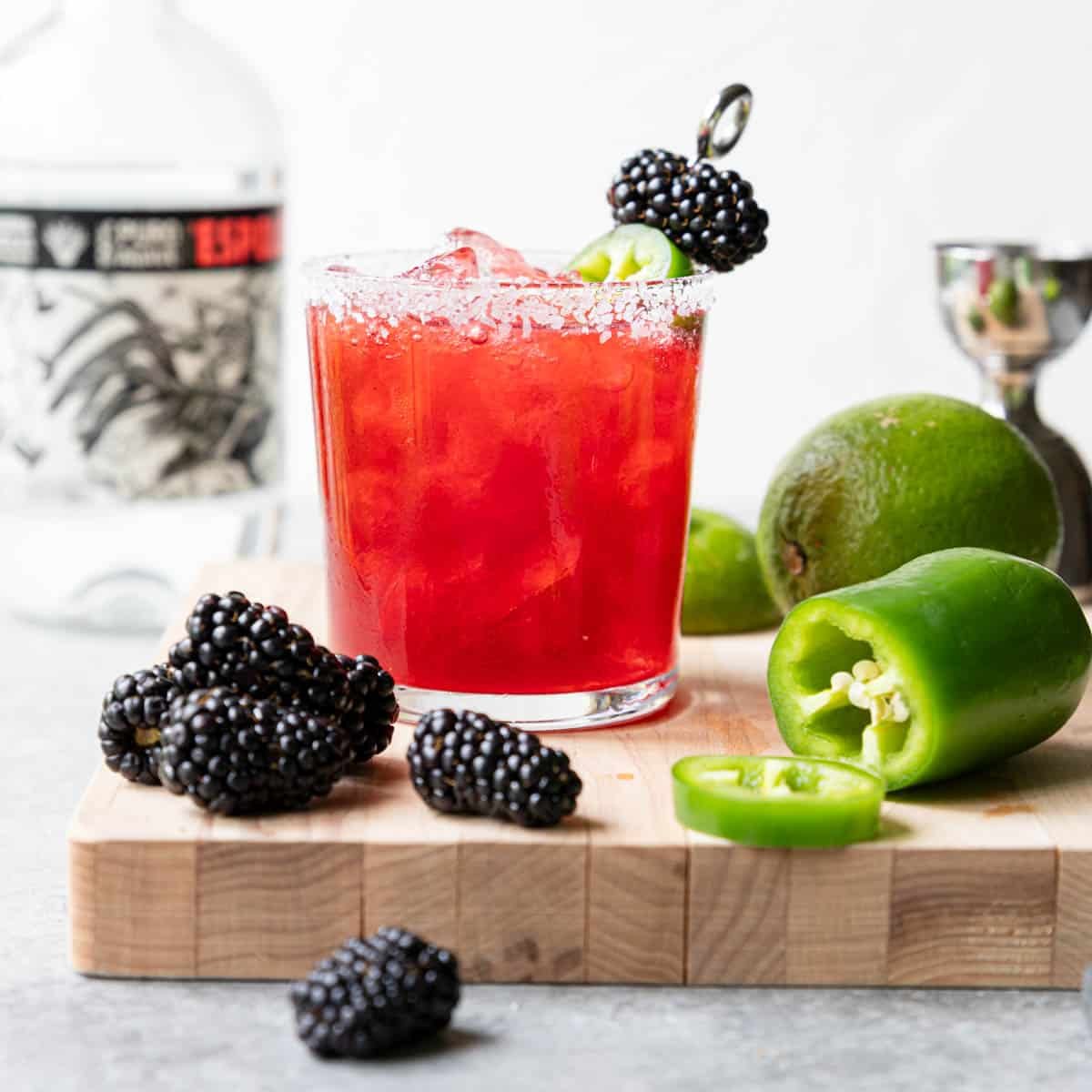 A glass with a salt rim filled with spicy blackberry margarita with a jalapeno and fresh blackberries to the side