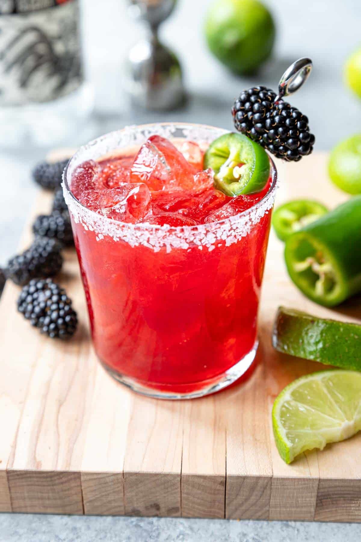 a salt rimmed glass with a spicy blackberry margarita, garnished with blackberries and jalapeno slice