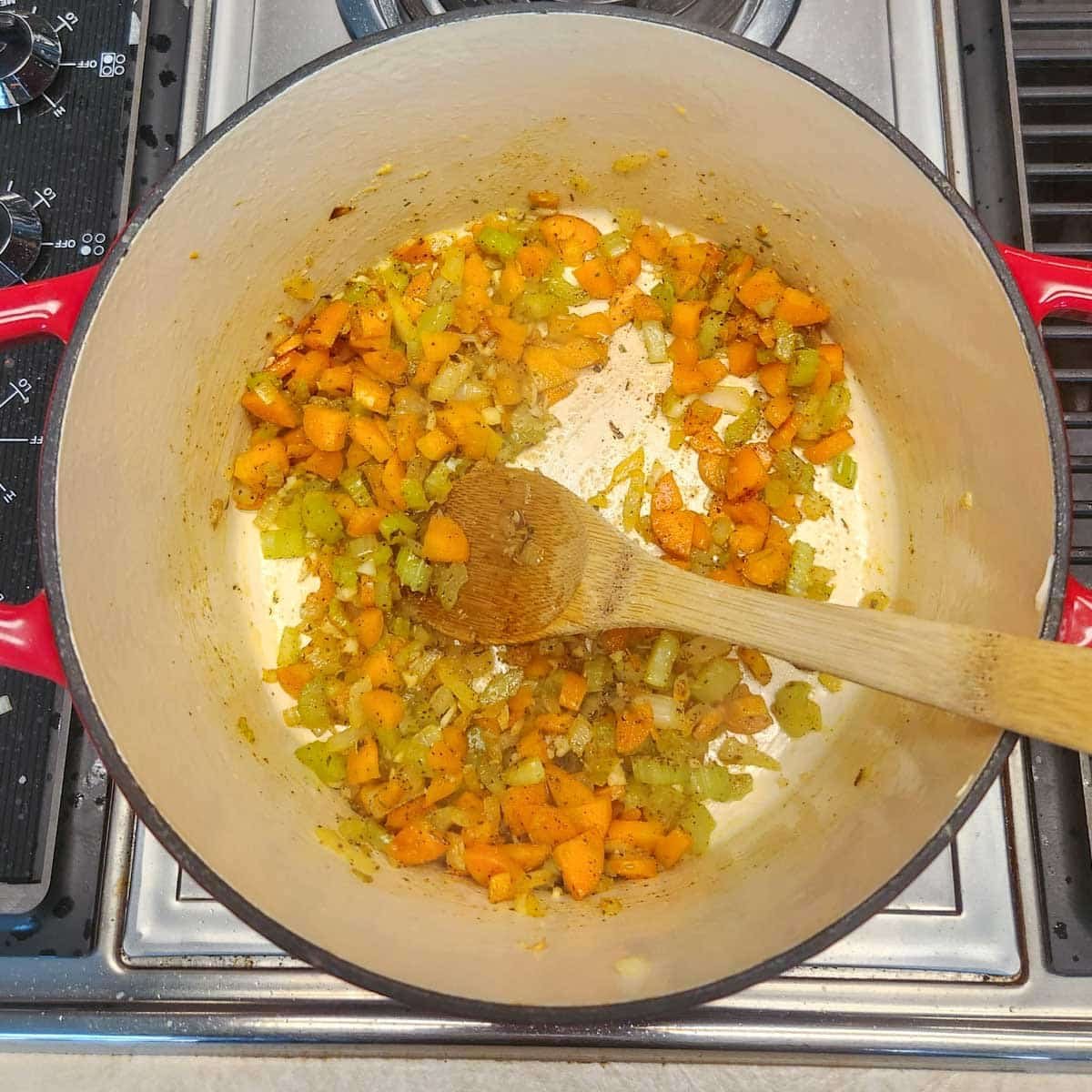 carrots, celery and onions in a Dutch Oven pot with a wooden spoon