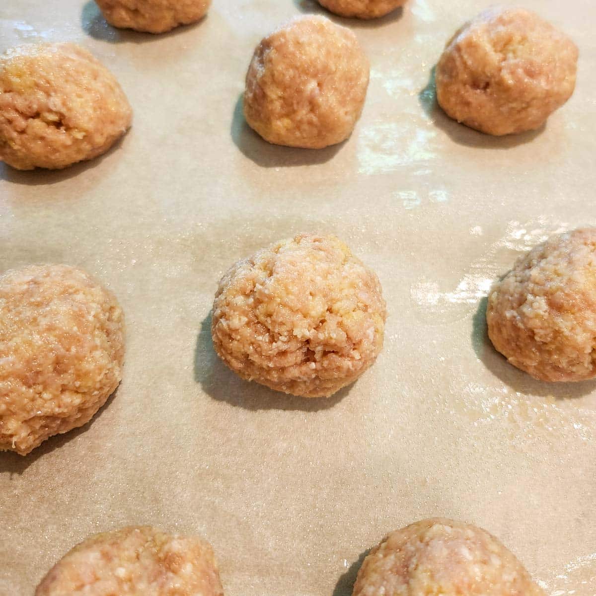 chicken meatballs rolled on a baking sheet on top of parchment 