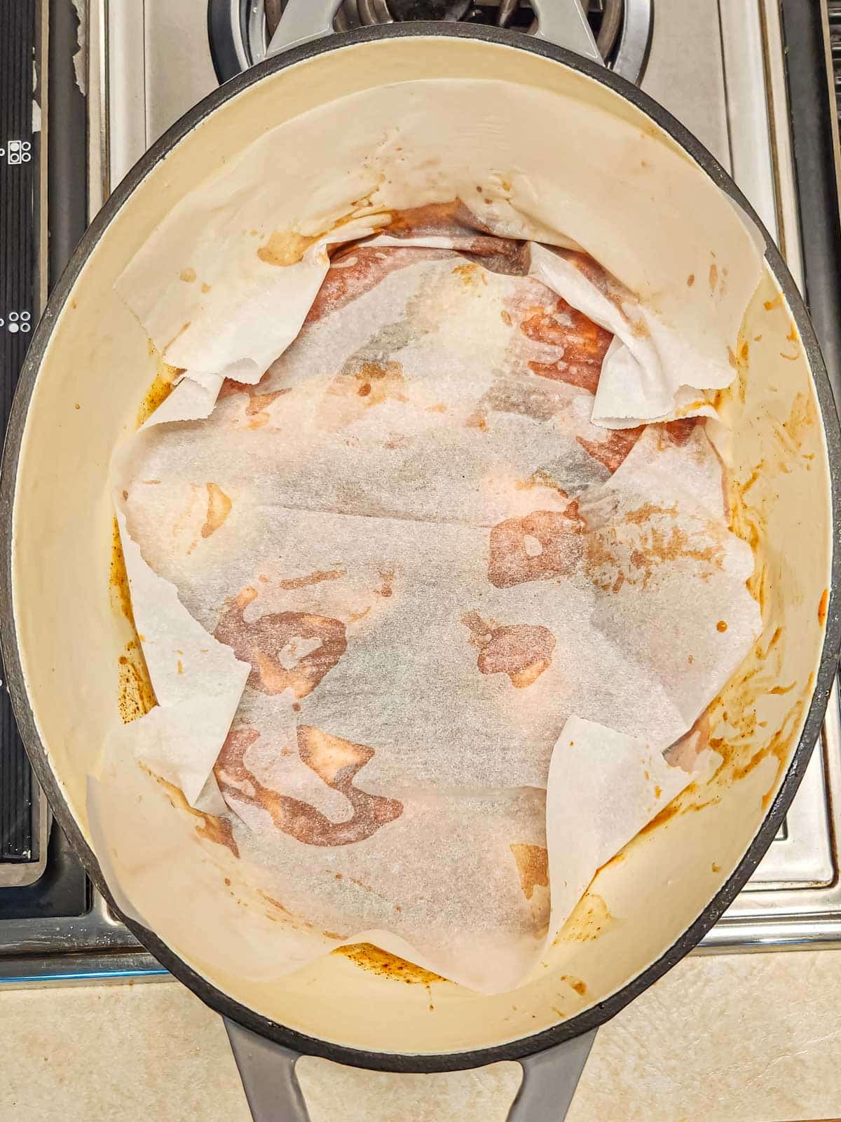 parchment covering boneless ribs in braising liquid in a Dutch Oven