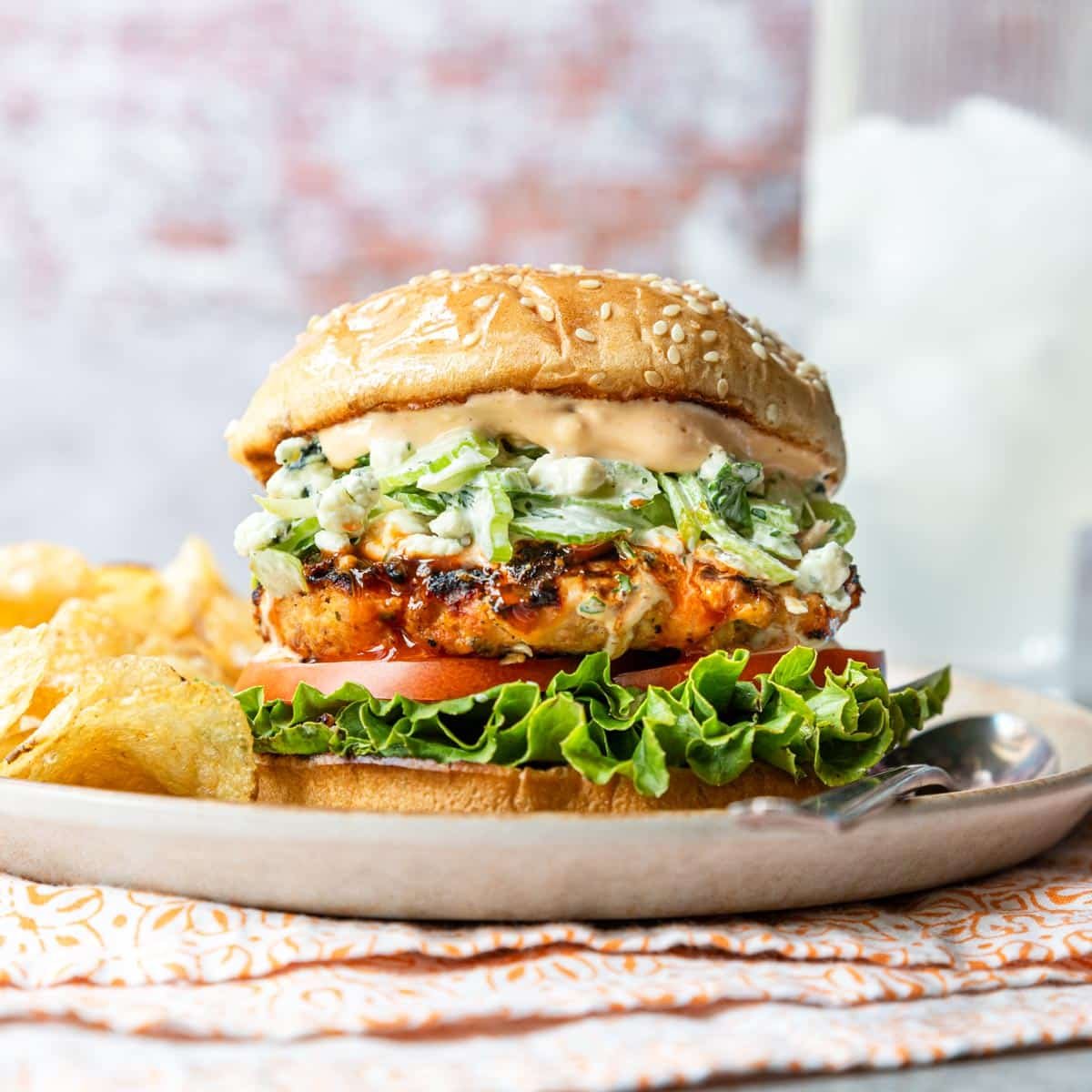 Buffalo chicken burger on a sesame seed bun with buffalo aioli and celery blue cheese slaw with kettle chips on the side.