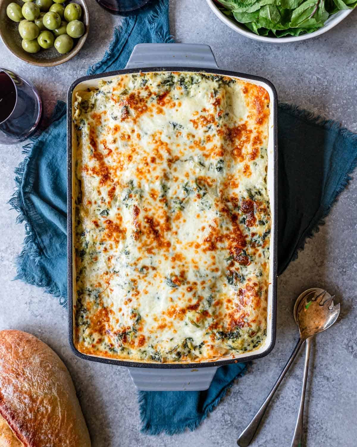 Top view of a freshly baked deluxe chicken lasagna in a baking dish with a loaf of bread ready to serve with it.